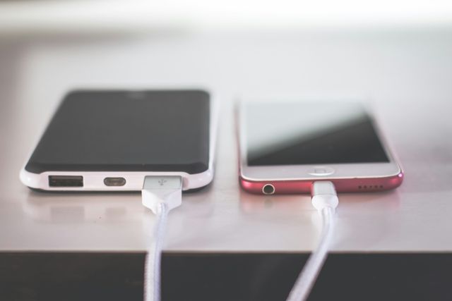 A power bank and a phone side by side on a table, both plugged in with charging cables.