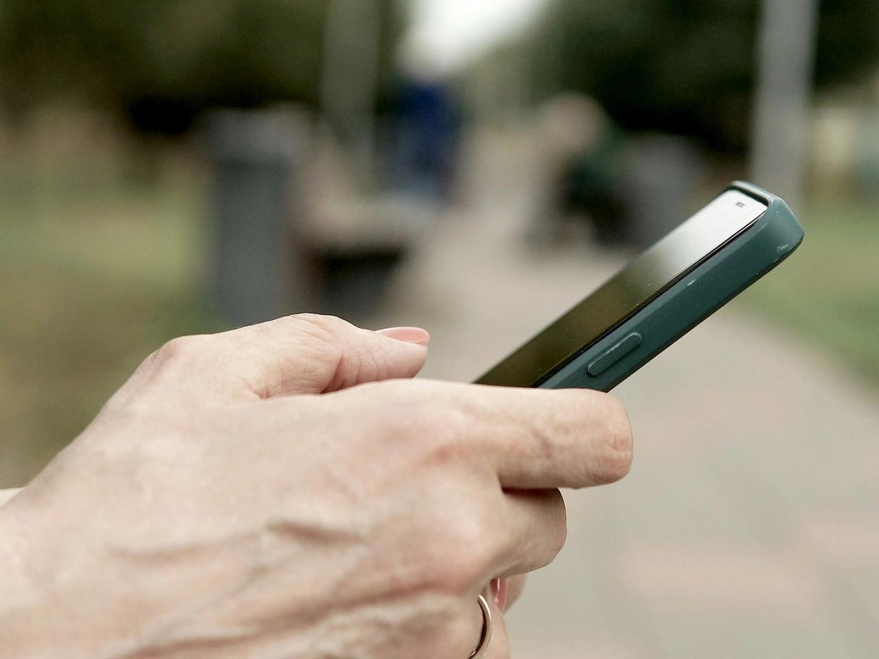 A hand holding a smartphone outdoors.