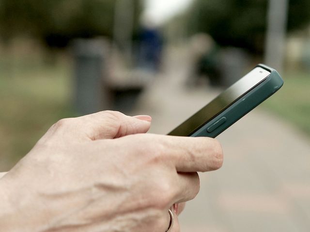 A hand holding a smartphone outdoors.