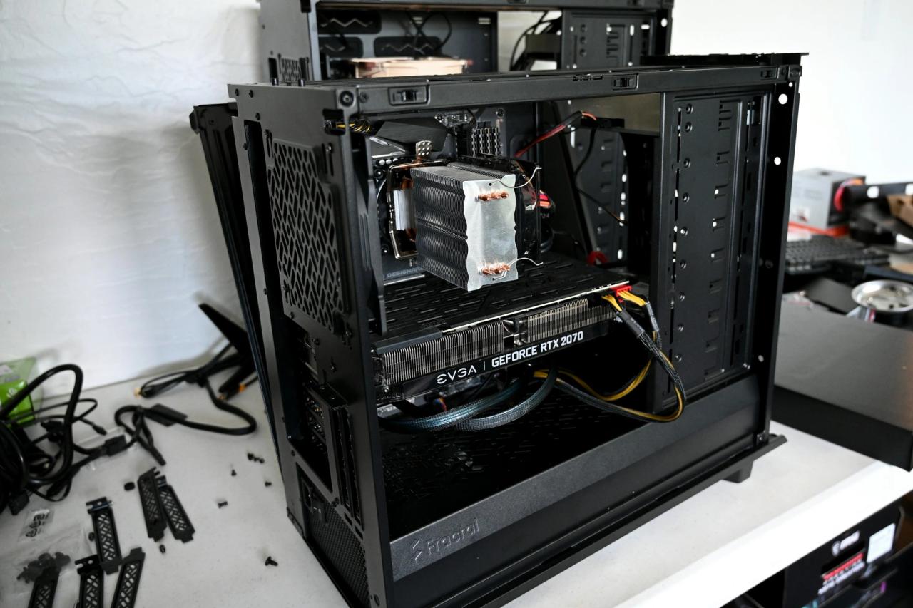 An open black PC case on a desk, with the graphics card, cooler and cables being fitted.