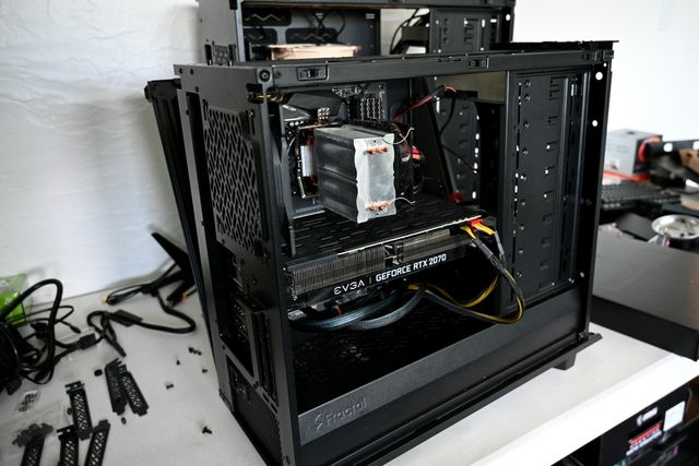 An open black PC case on a desk, with the graphics card, cooler and cables being fitted.