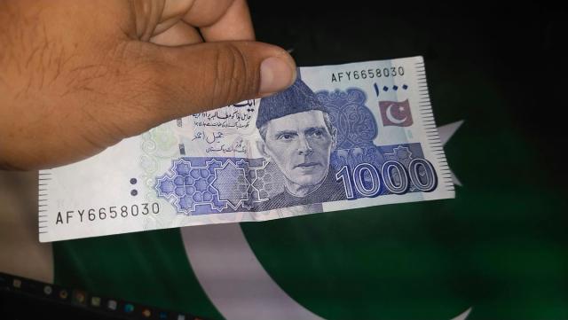 A hand holding a Pakistani 1,000 rupee note.