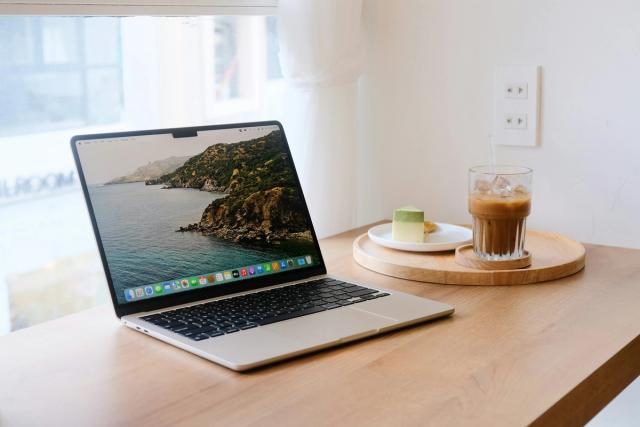 A MacBook open on a wooden table next to a cup of iced coffee.