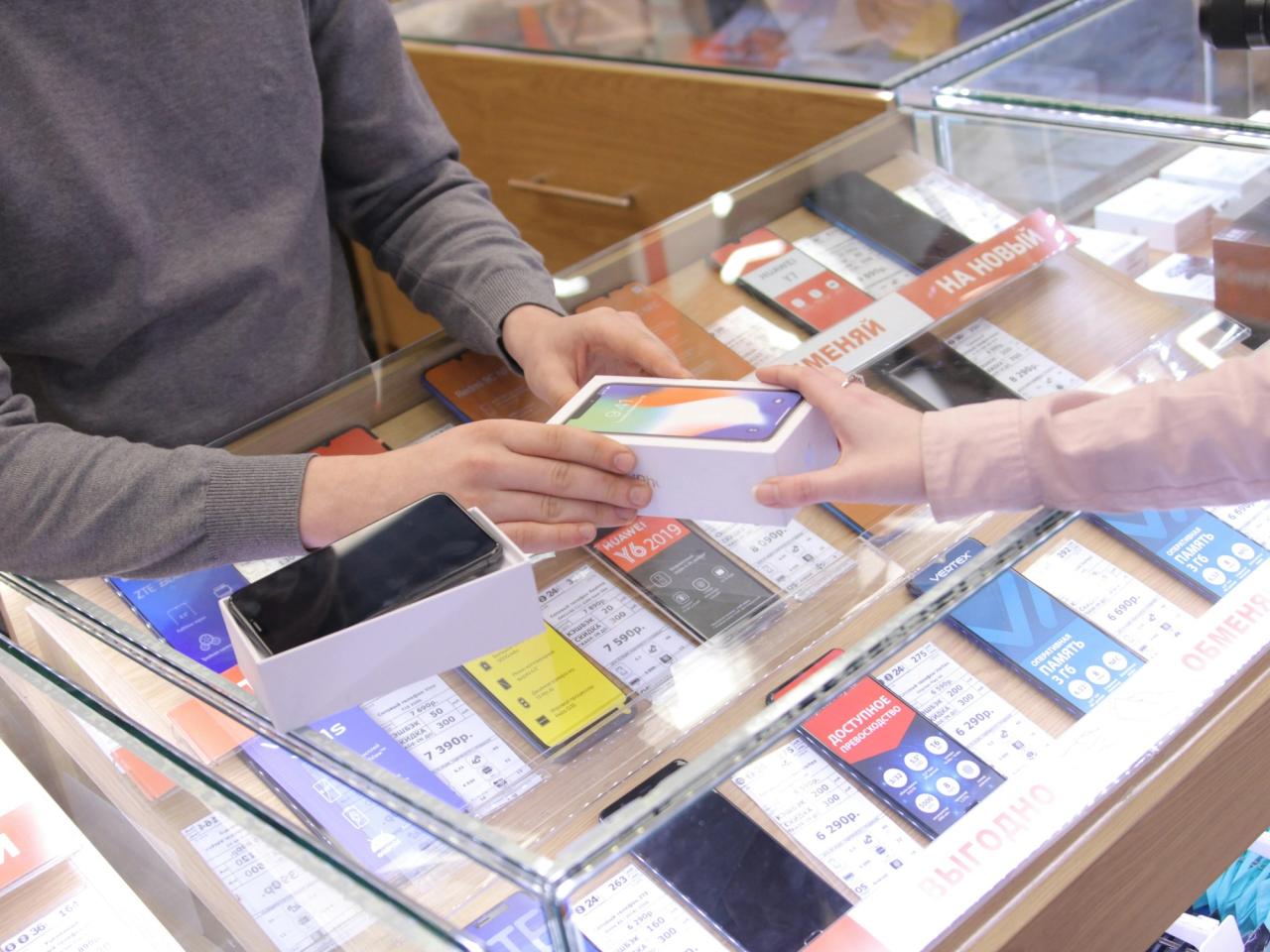 A customer and a shop assistant passing a phone across a mobile shop counter.
