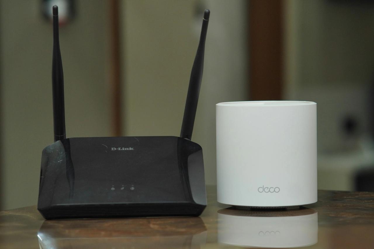 A traditional WiFi router with antennas next to a small white mesh WiFi unit on a table.