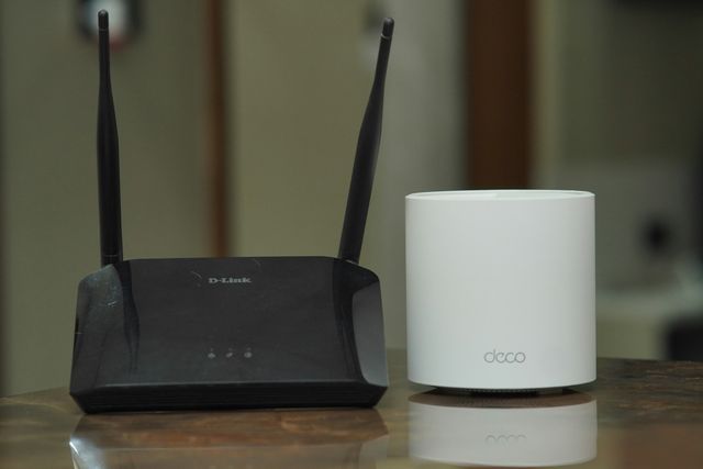 A traditional WiFi router with antennas next to a small white mesh WiFi unit on a table.