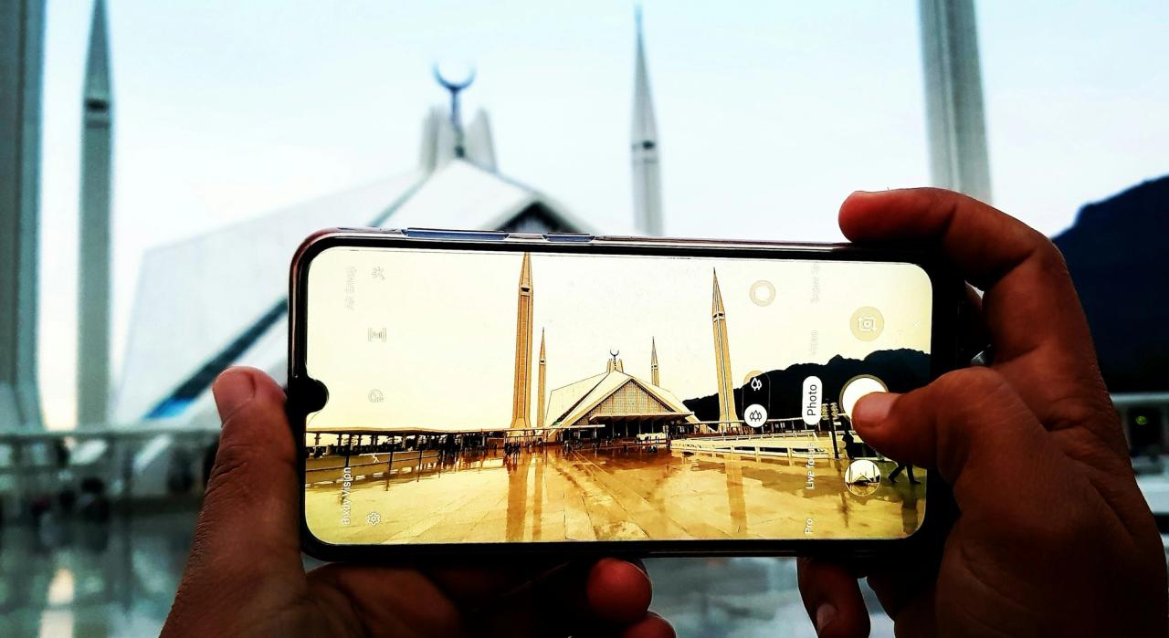 Hands holding a smartphone to photograph the Faisal Mosque in Islamabad.