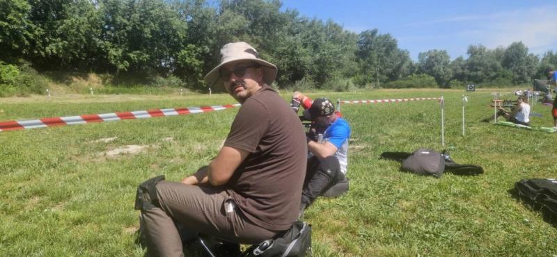 Takmičar u šeširu na stajalištu, iza njega strelci na stazi