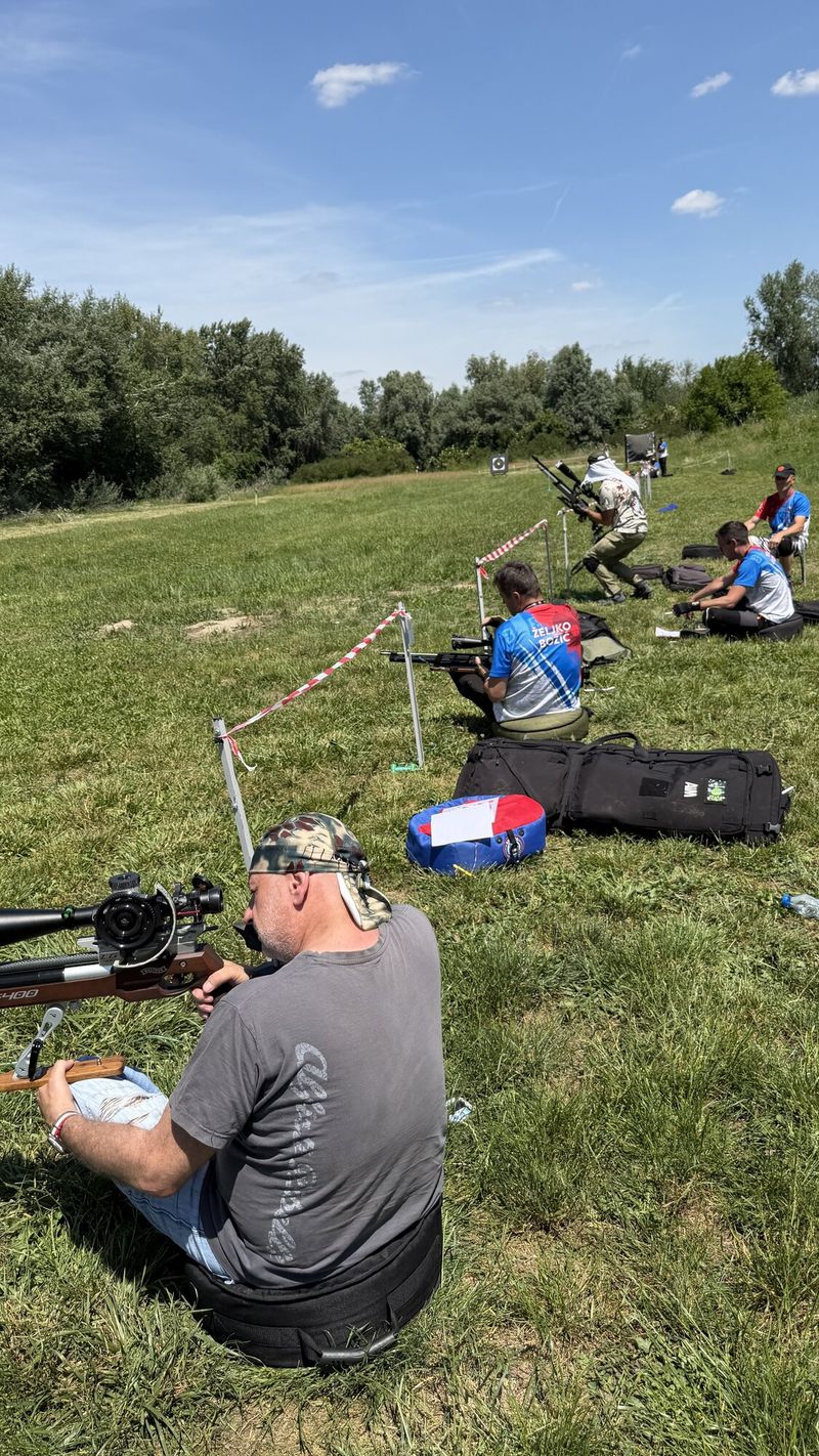 Takmičar gađa iz sedećeg položaja na otvorenoj livadi