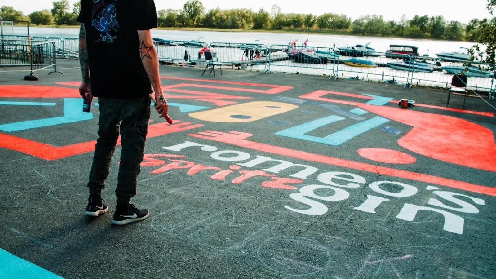 Romeo's Spritz Gin hand-painted lettering across the marina ground, painter standing on the letters