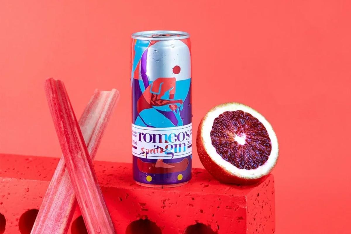 Romeo's Gin Spritz can on red, blood orange cut beside it — the wall artwork living on the shelf