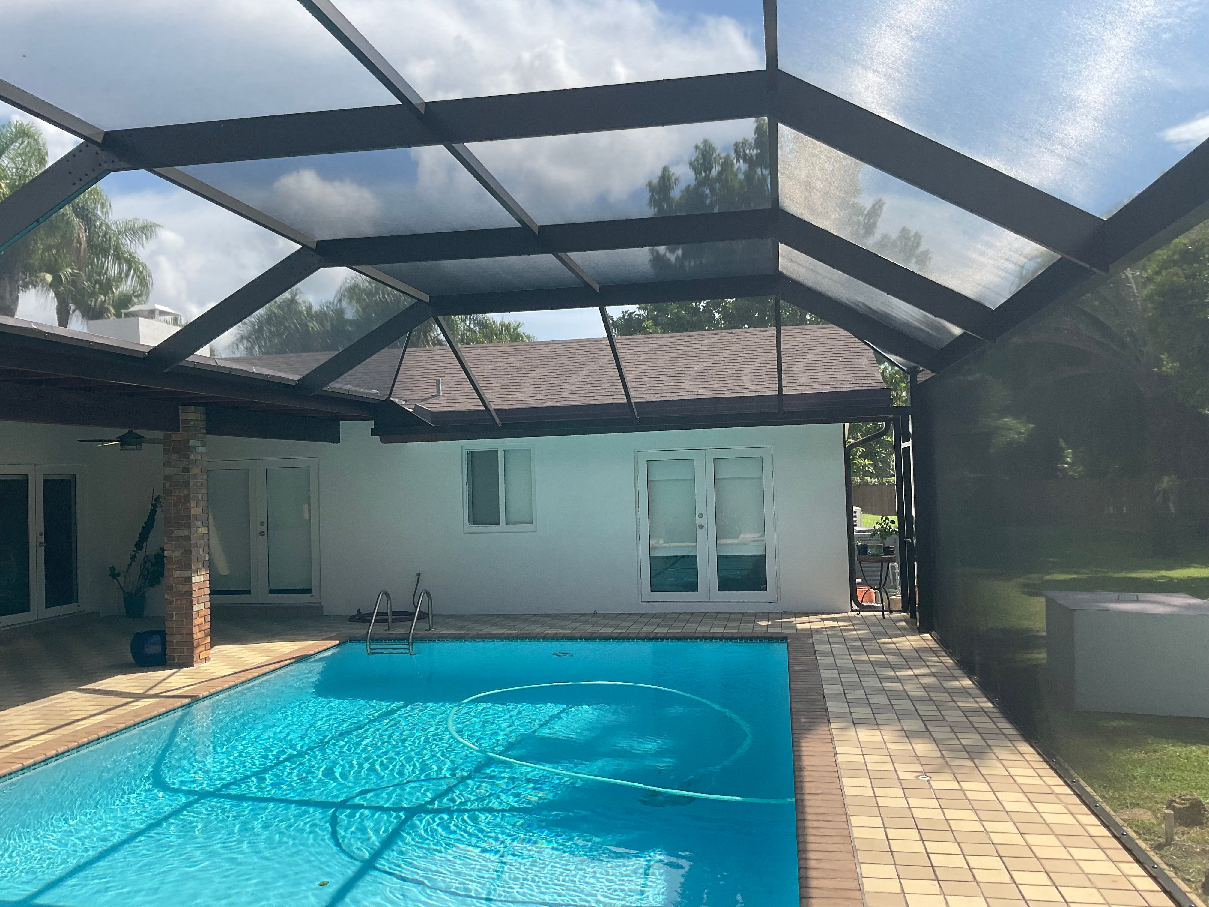 Dark bronze aluminum pool screen enclosure interior, rectangular pool with tile deck and French doors, stucco home, South Florida — AB Aluminum & Screens