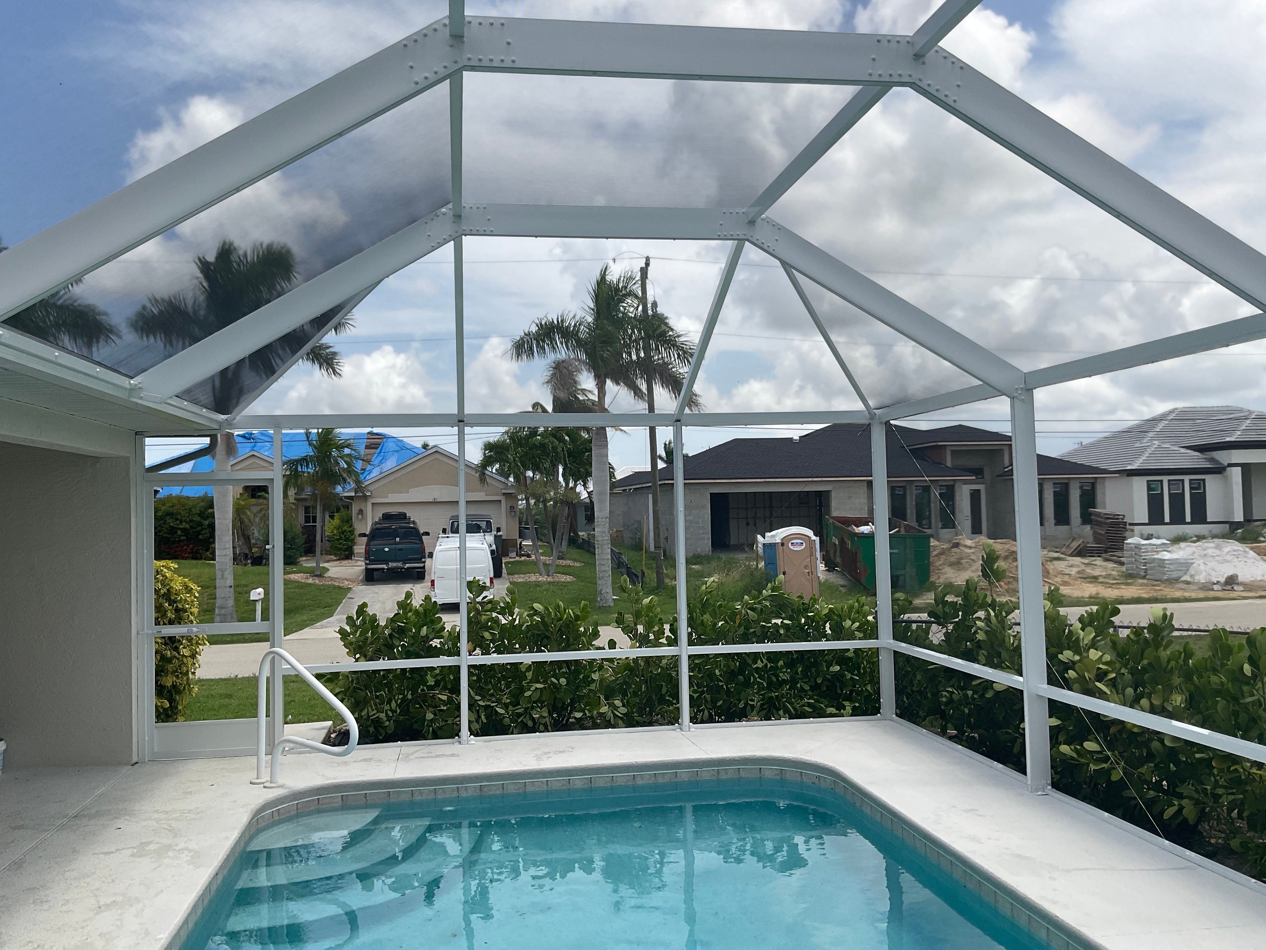 Interior of white aluminum pool screen enclosure overlooking residential neighborhood with construction and palm trees — AB Aluminum & Screens