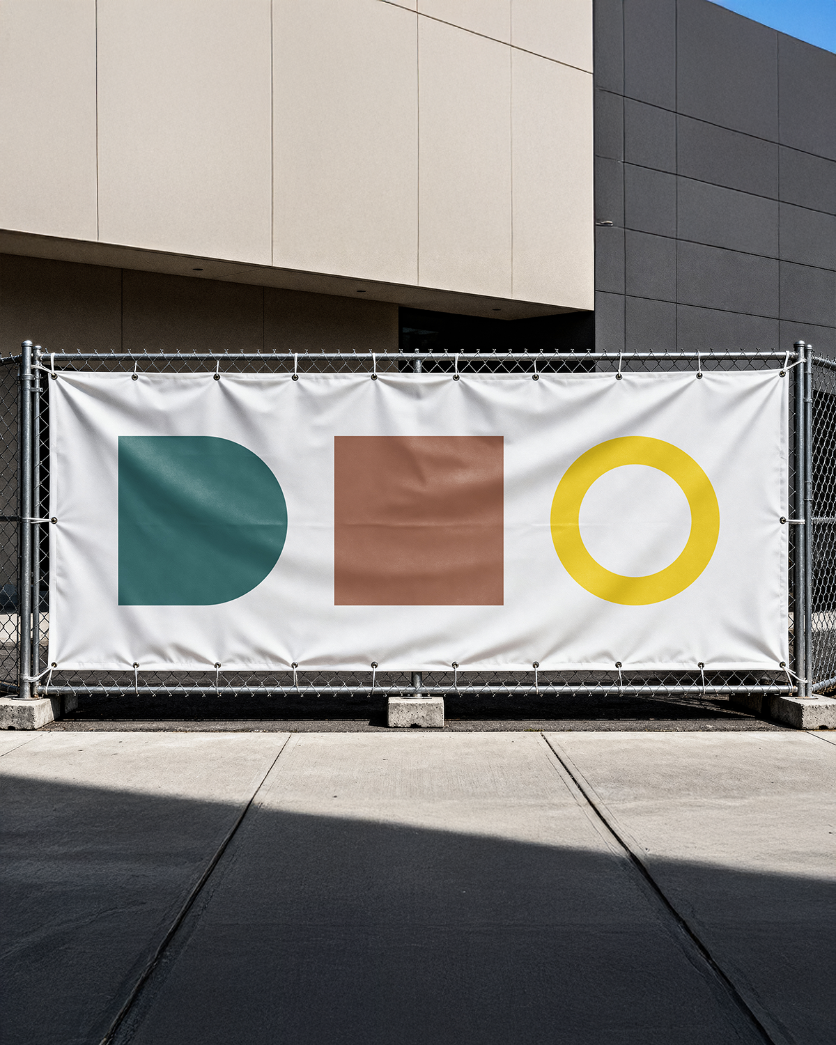 Een witte werfbanner aan een heras. Hierop staan 3 simpele symbolen. Het eerste is een vierkant waar de rechterkant afgrond is in een donkergroen kleur, Daarnaast in het midden een bruine vierkant en als laatste een cirkel waar enkel de stoke getoond wordt in het geel.