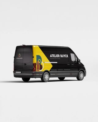 Camionette met aan de zijkant een gele driehoek die naar de neus van de auto wijst. Op het gele vlak het logo van Atelier Buyck. Naast het gele vlak de naam Atelier Buyck voluit geschreven onderaan de zijkant alle informatie.