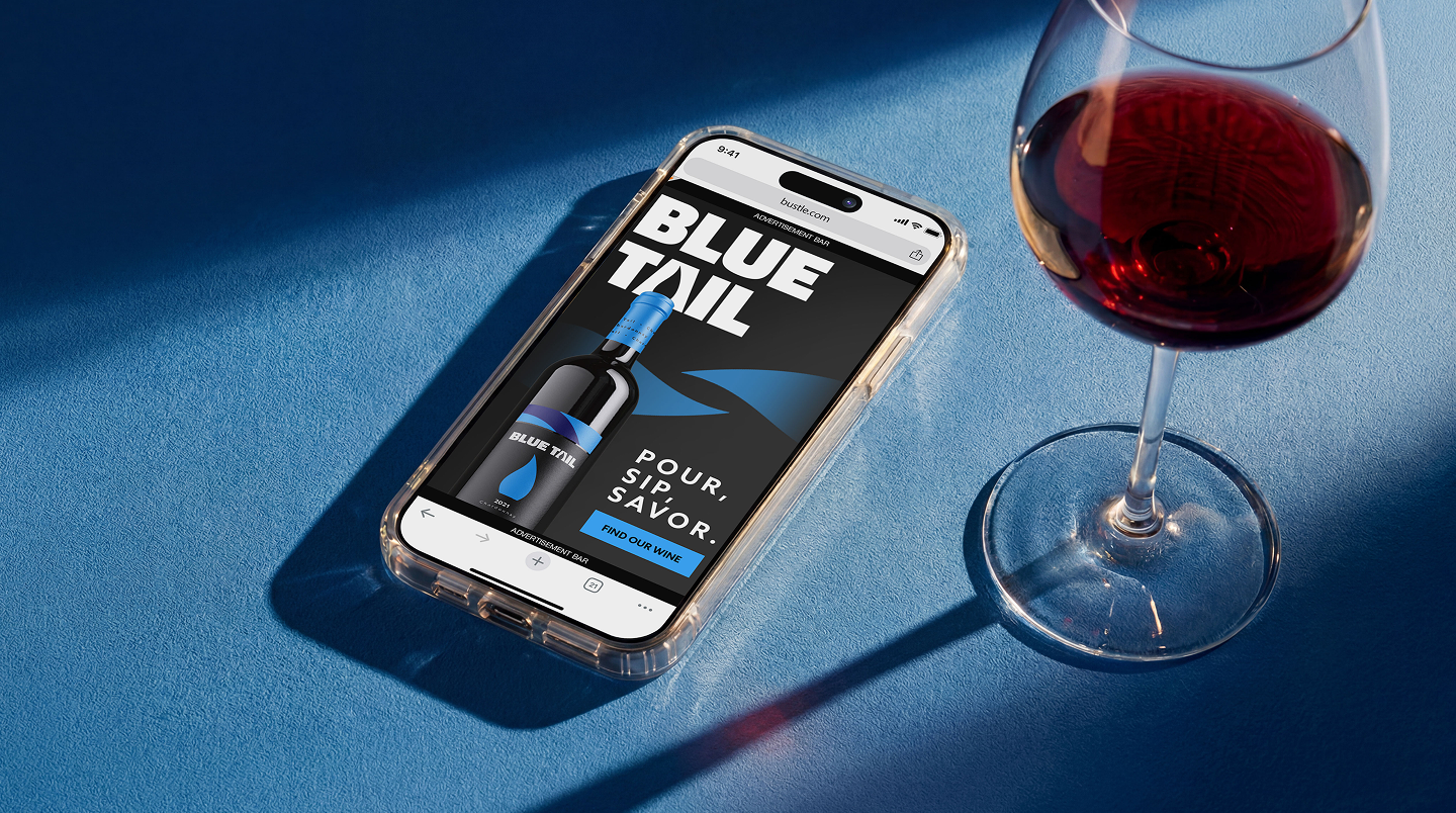 A smartphone displaying a Blue Tail wine ad sits beside a glass of red wine on a blue surface.
