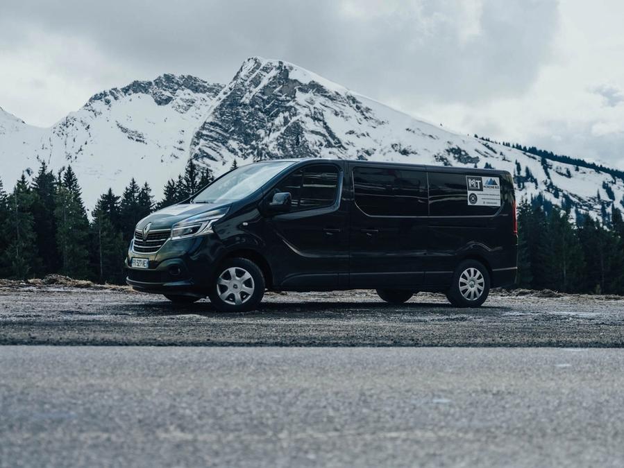 Black Renault Trafic 8-seat minibus side on, with snow-capped mountains behind