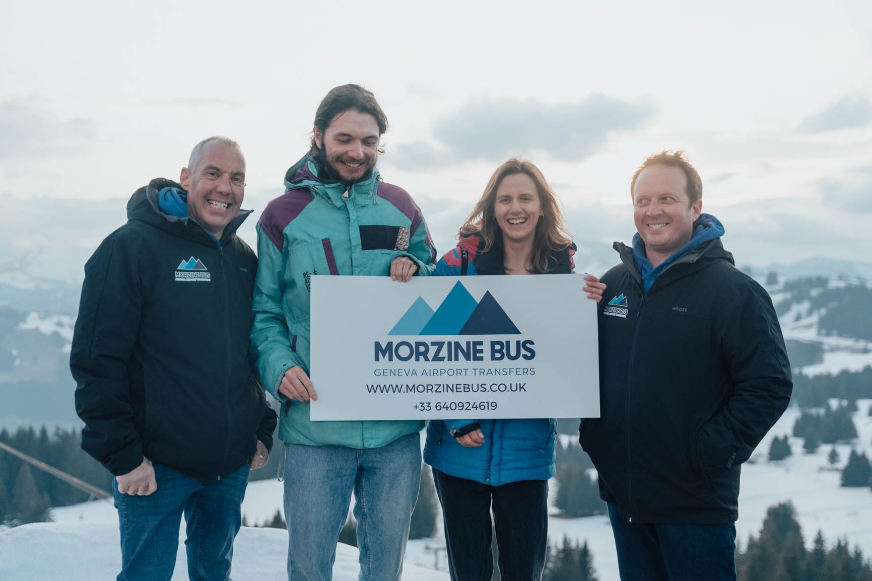 The Morzine Bus team holding a Morzine Bus sign in the snow