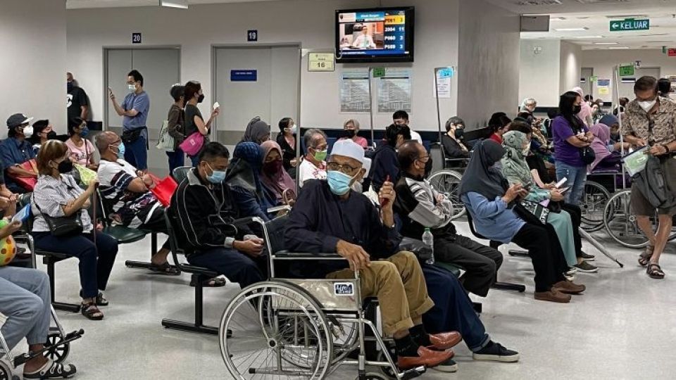 A crowded hospital waiting room with masked people, including some in wheelchairs.