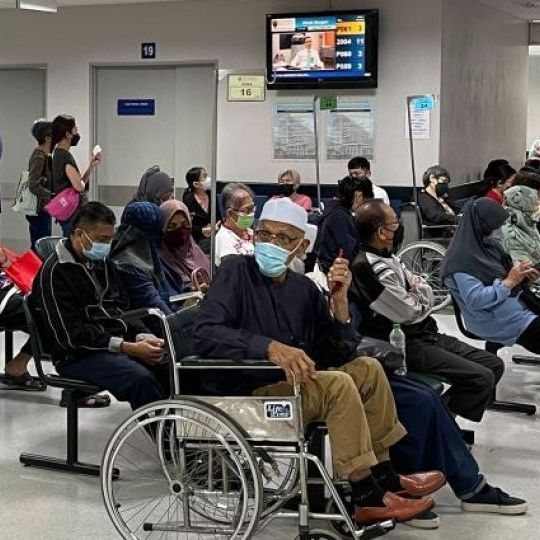 A crowded hospital waiting room with masked people, including some in wheelchairs.