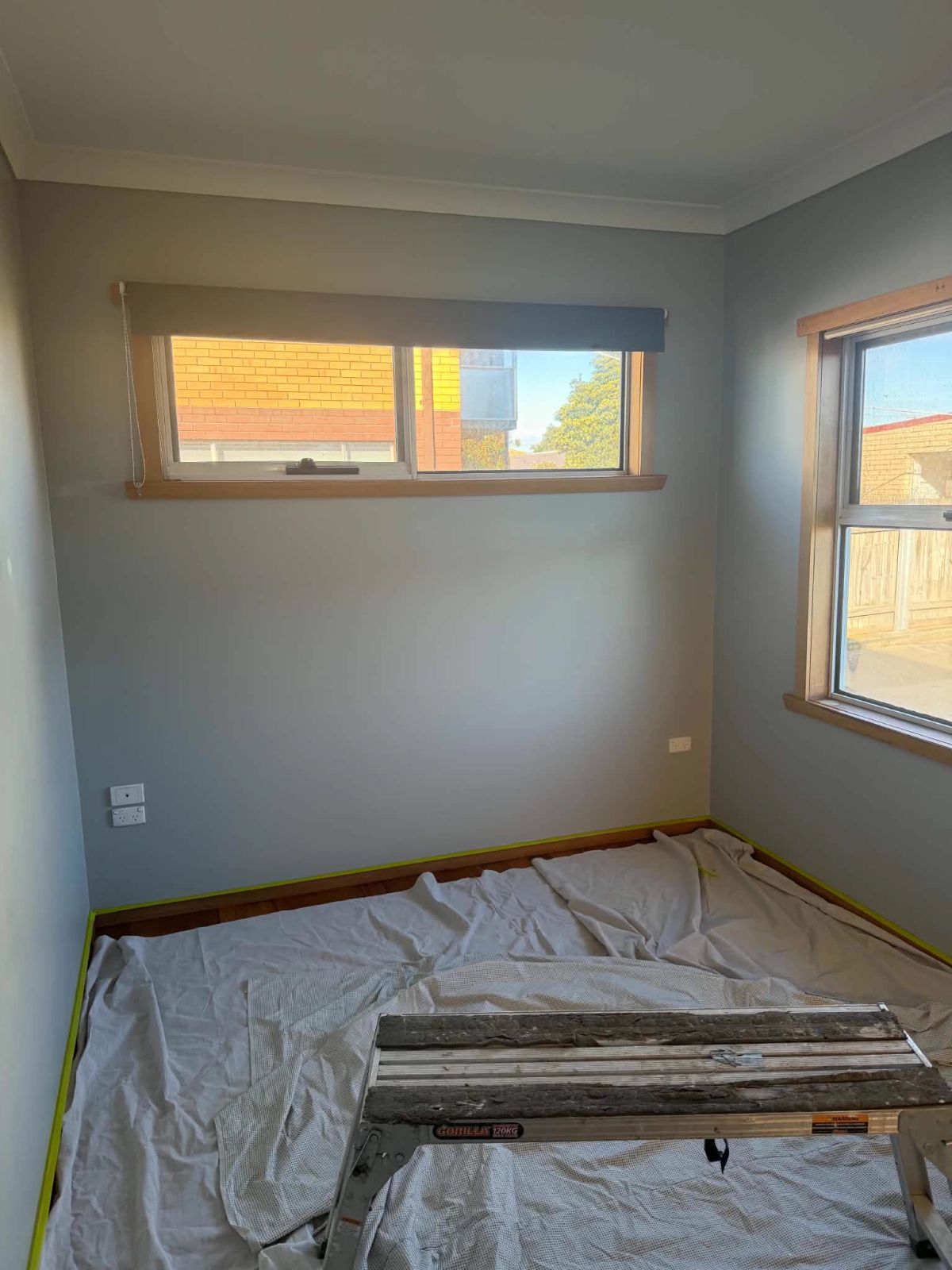 Bedroom before the repaint: grey walls, floor covered and edges taped
