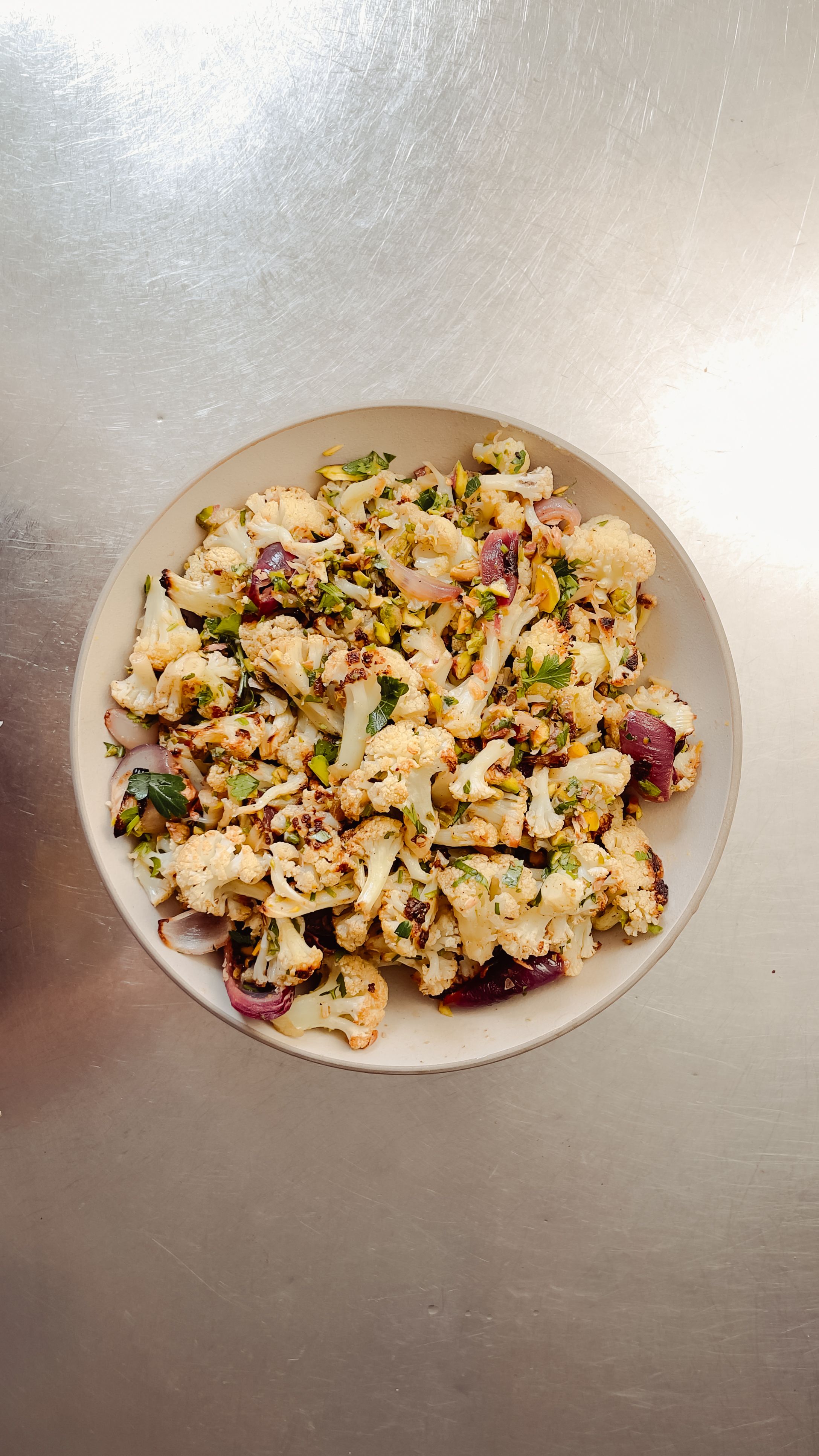tangy roasted cauliflower in a ceramic bowl on a stainless steel table