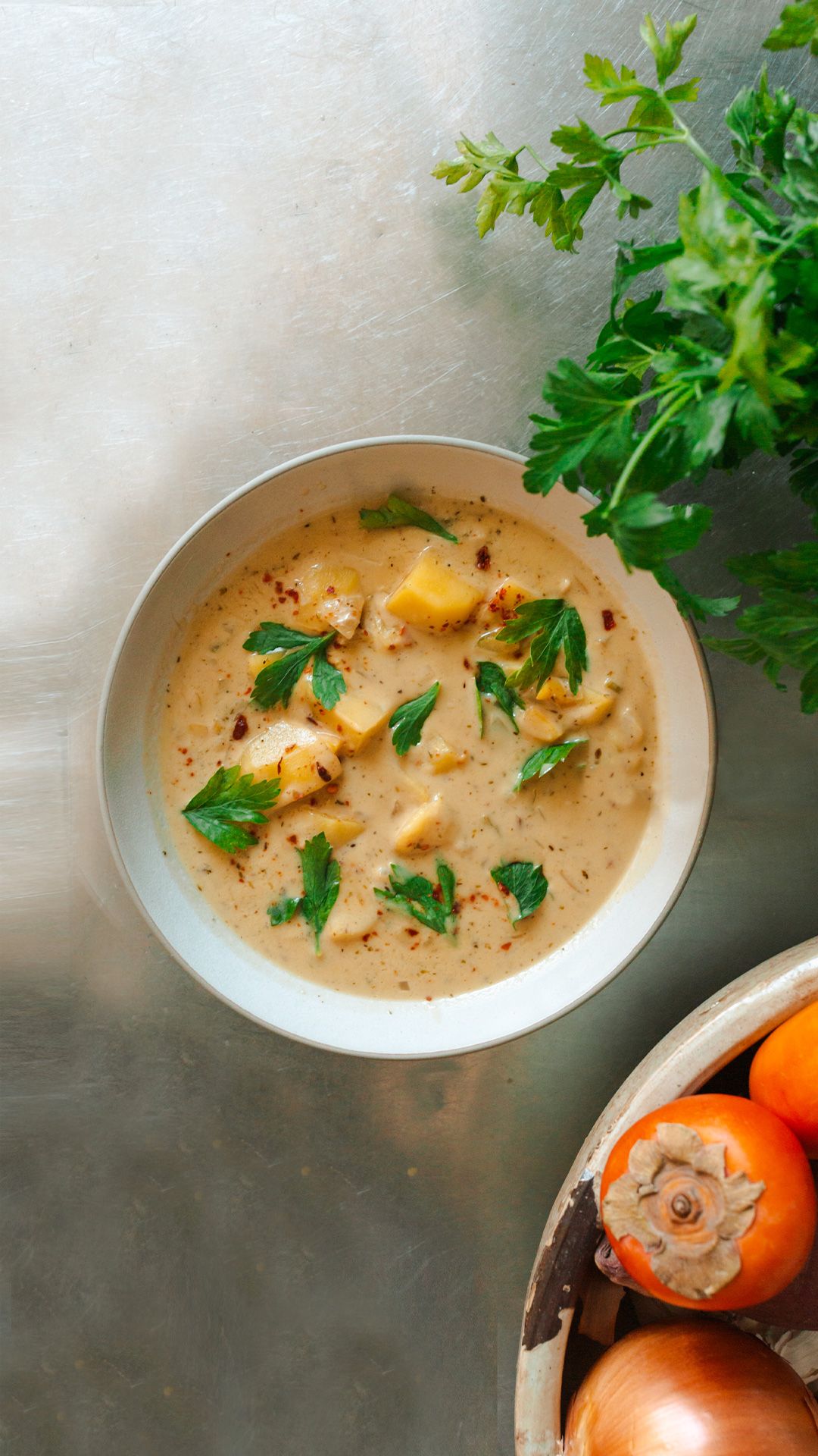 creamy coconut potato soup on a stainless steel table near some persimmons