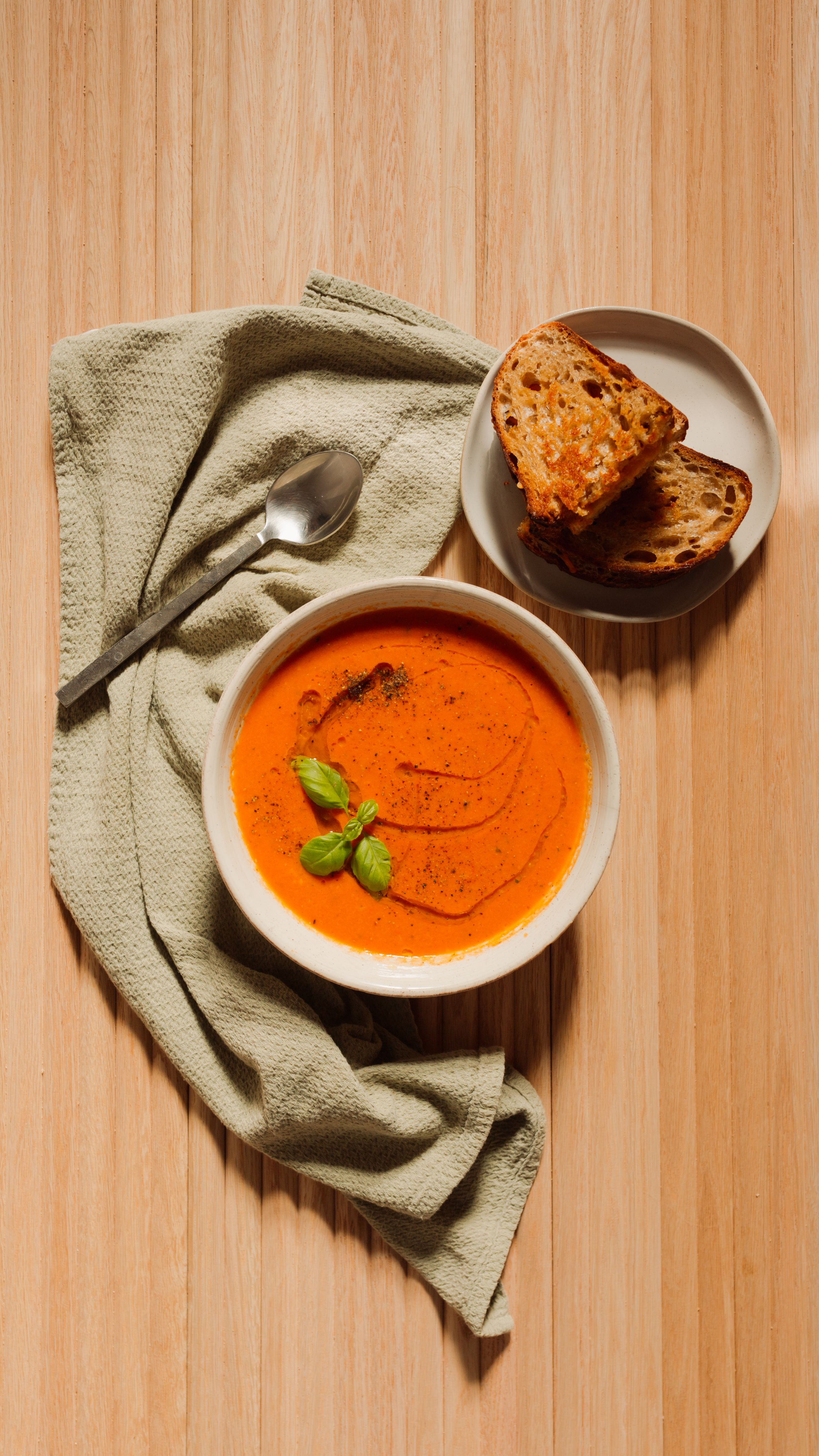 tomato soup and grilled cheese on a wooden backdrop with a green tablecloth
