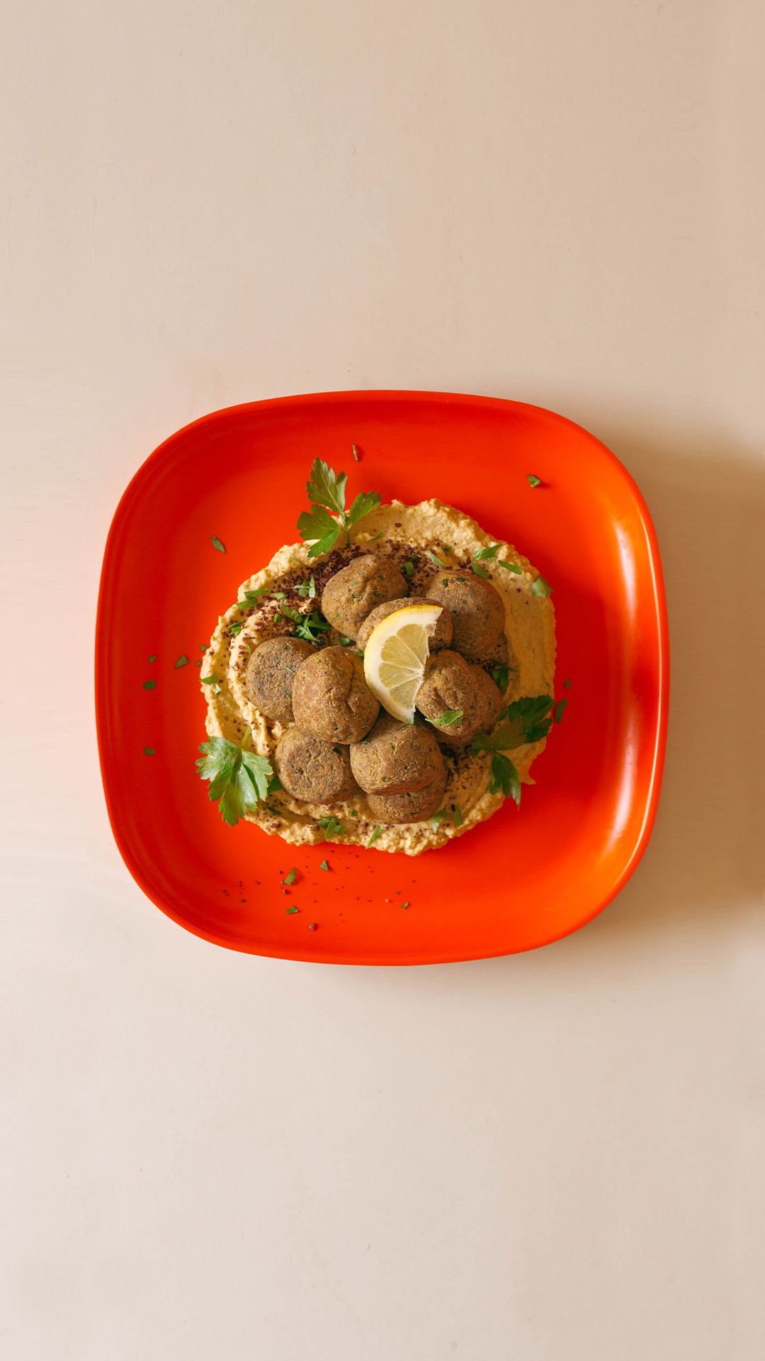 plant based meatballs inspired by middle eastern cuisine on a bed of hummus on a red plate