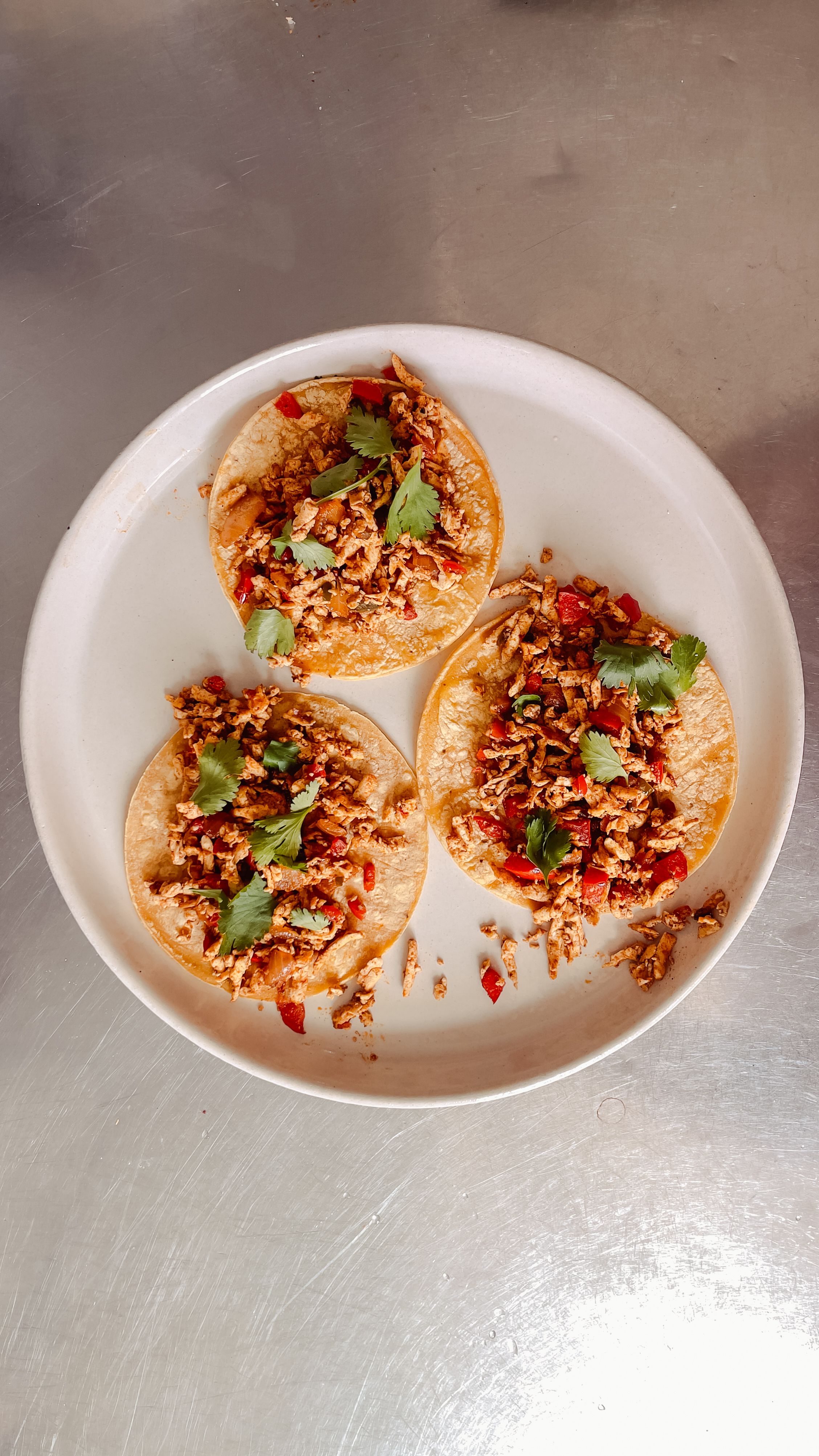 three shredded tofu tacos on a white plate on a steel tabletop