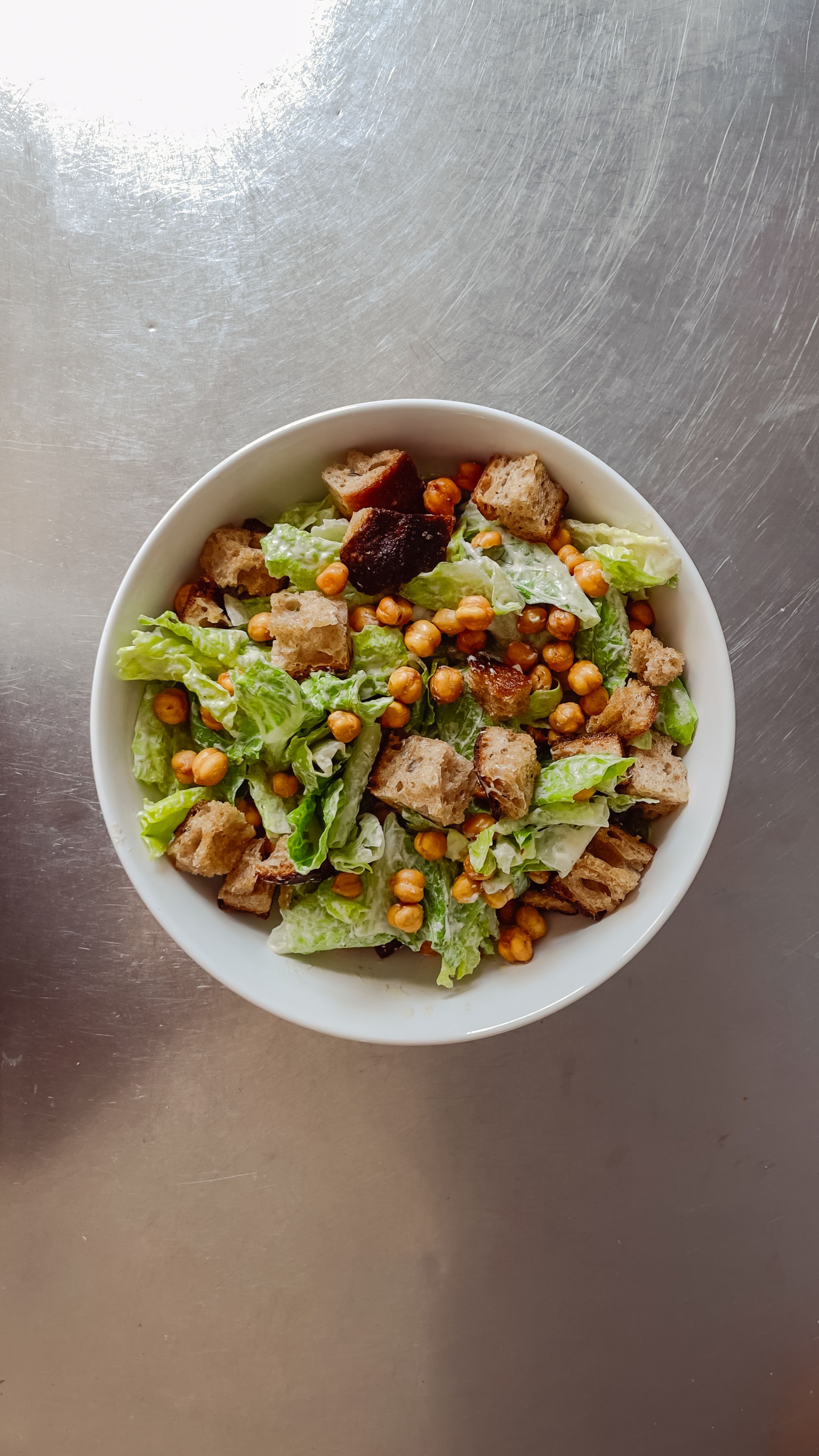 romaine lettuce with croutons and vegan caesar dressing in a bowl on a stainless steel countertop
