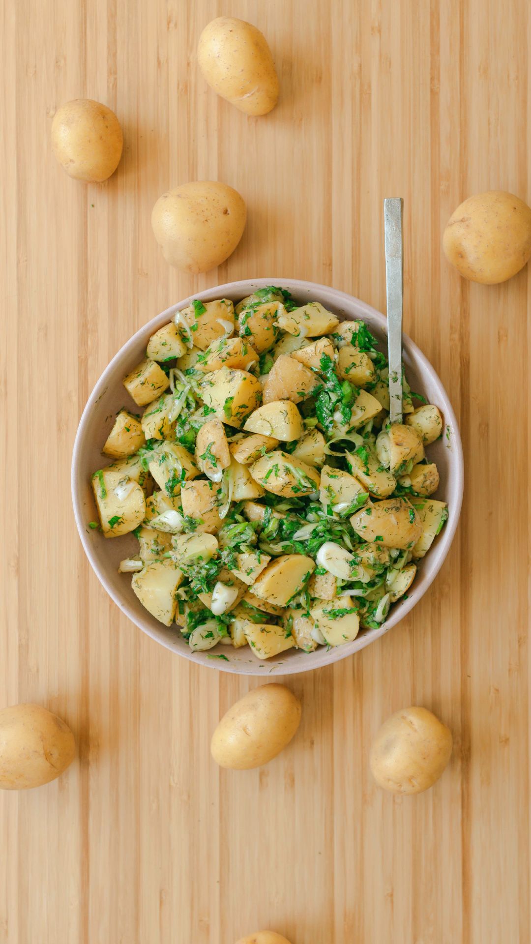 french-style potato salad in a bowl on a wooden tabletop with whole potatoes scattered around