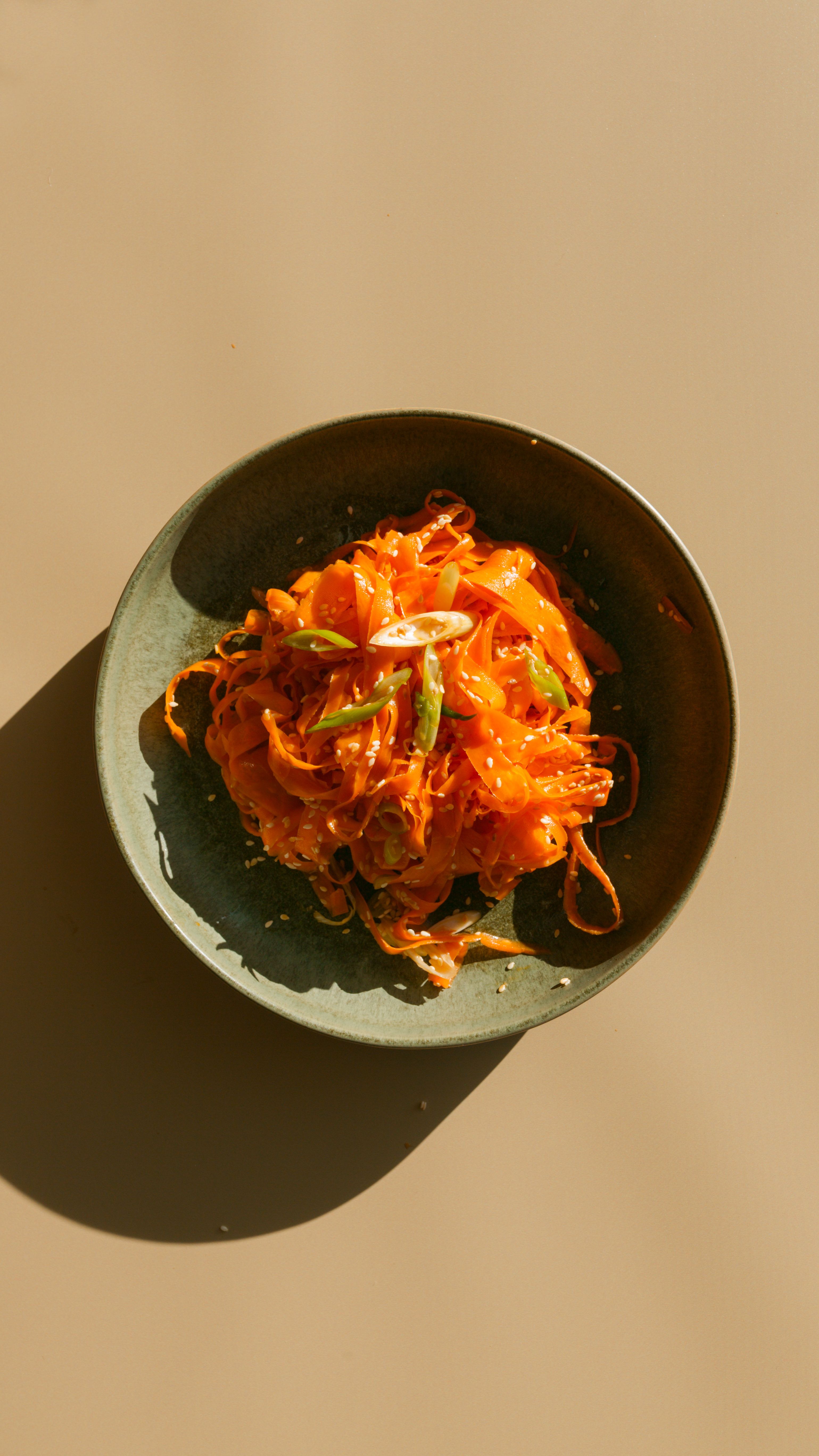carrot salad in a green bowl with an afternoon shadow