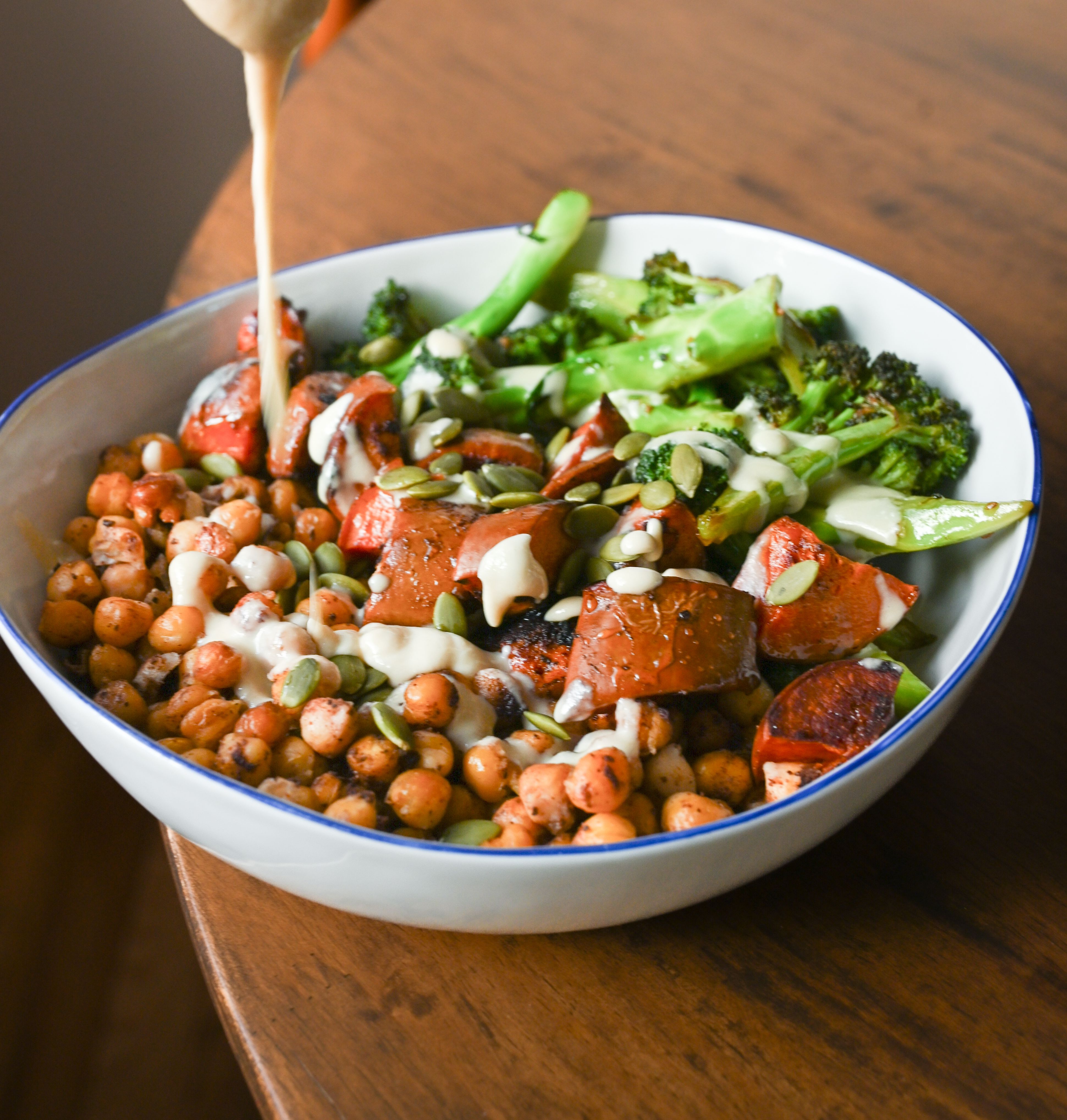 adding dressing to butternut squash bowl on wood kitchen table 