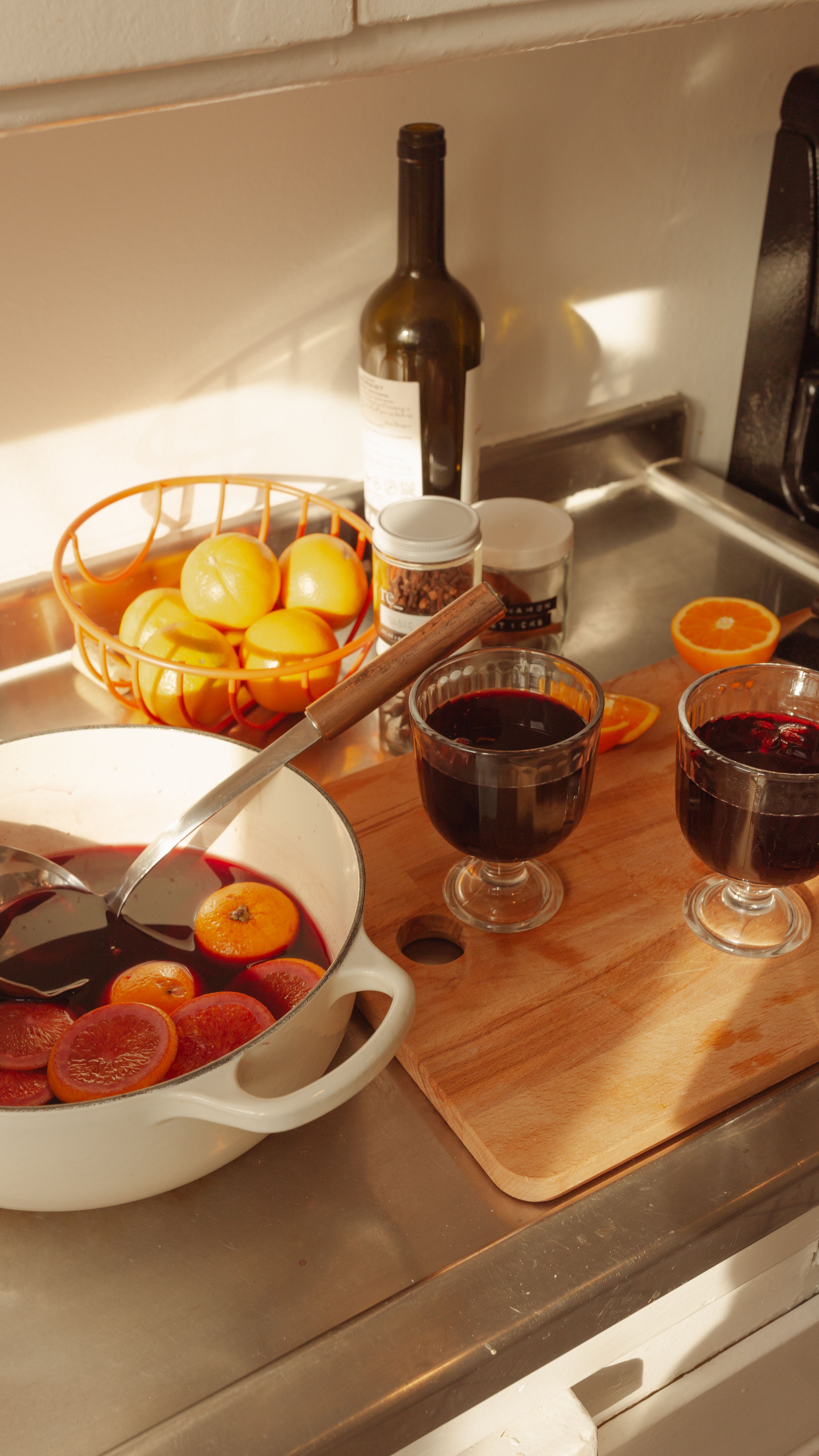 oranges in a bowl near a pot of mulled wine with glasses on a cutting board