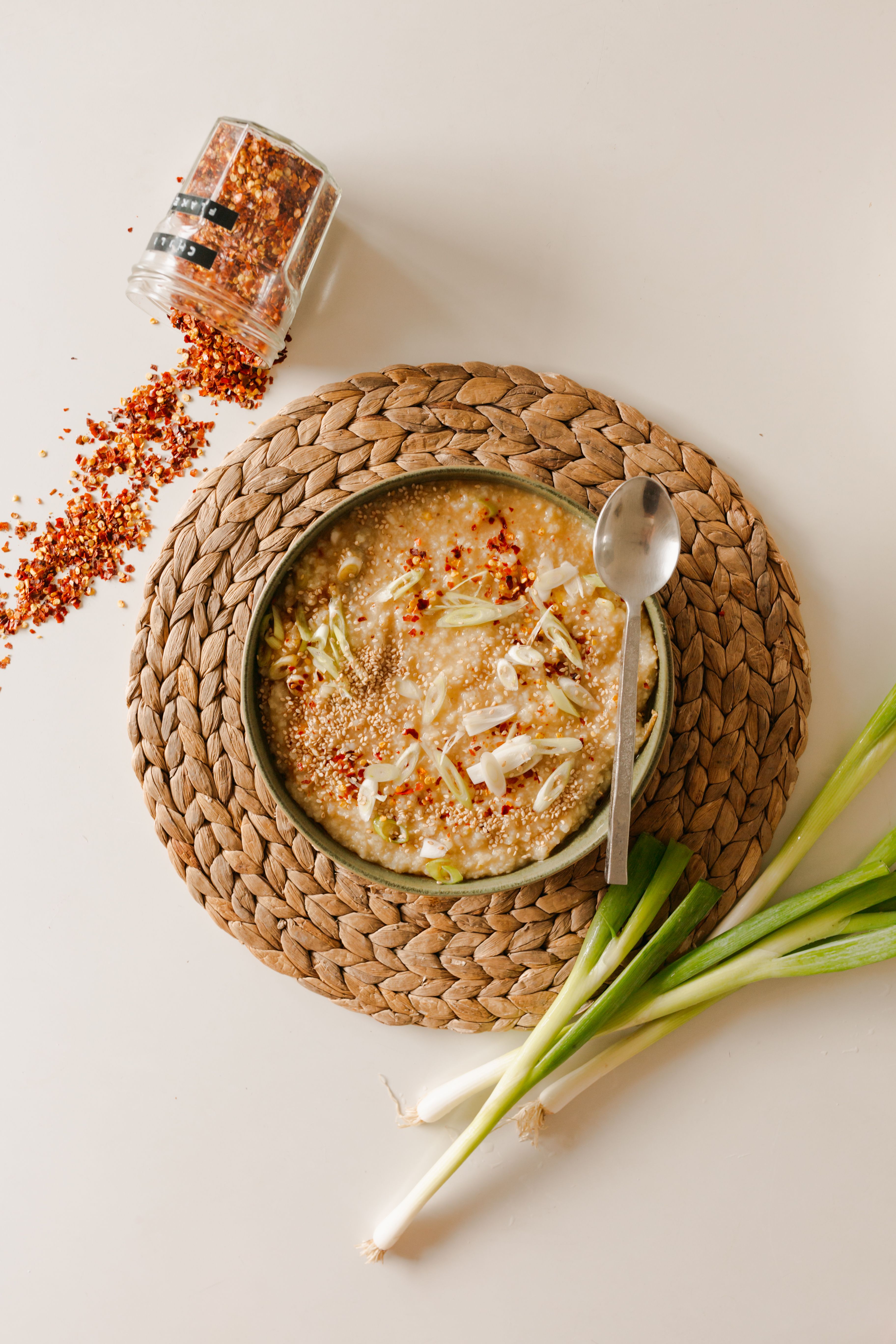 shiitake mushroom congee wtih green onion and chili flakes on a rattan placemat