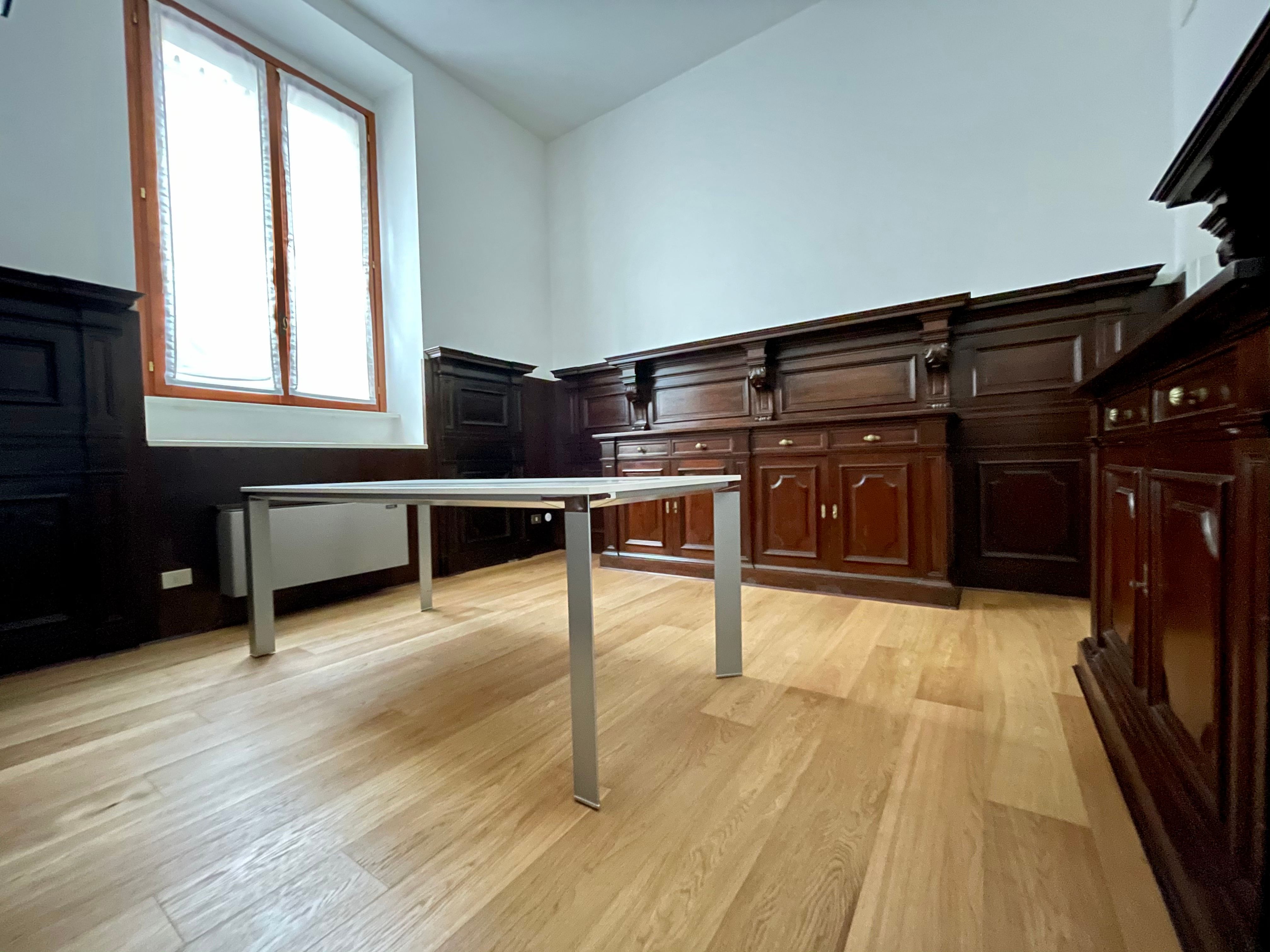 Uffico con parquet, pareti in legno scuro, finestra con tende, tavolo