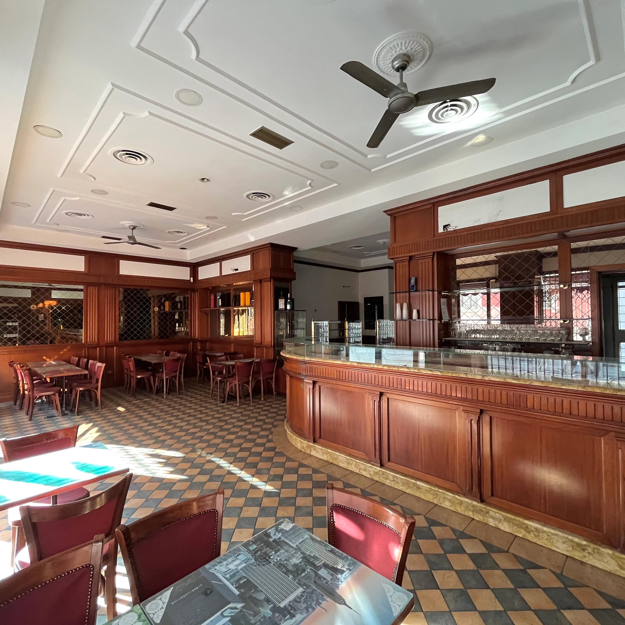 interno del bar, con bancone, vetrina, tavolini e sedie, specchi a parete, pale per ventilazione sul soffitto