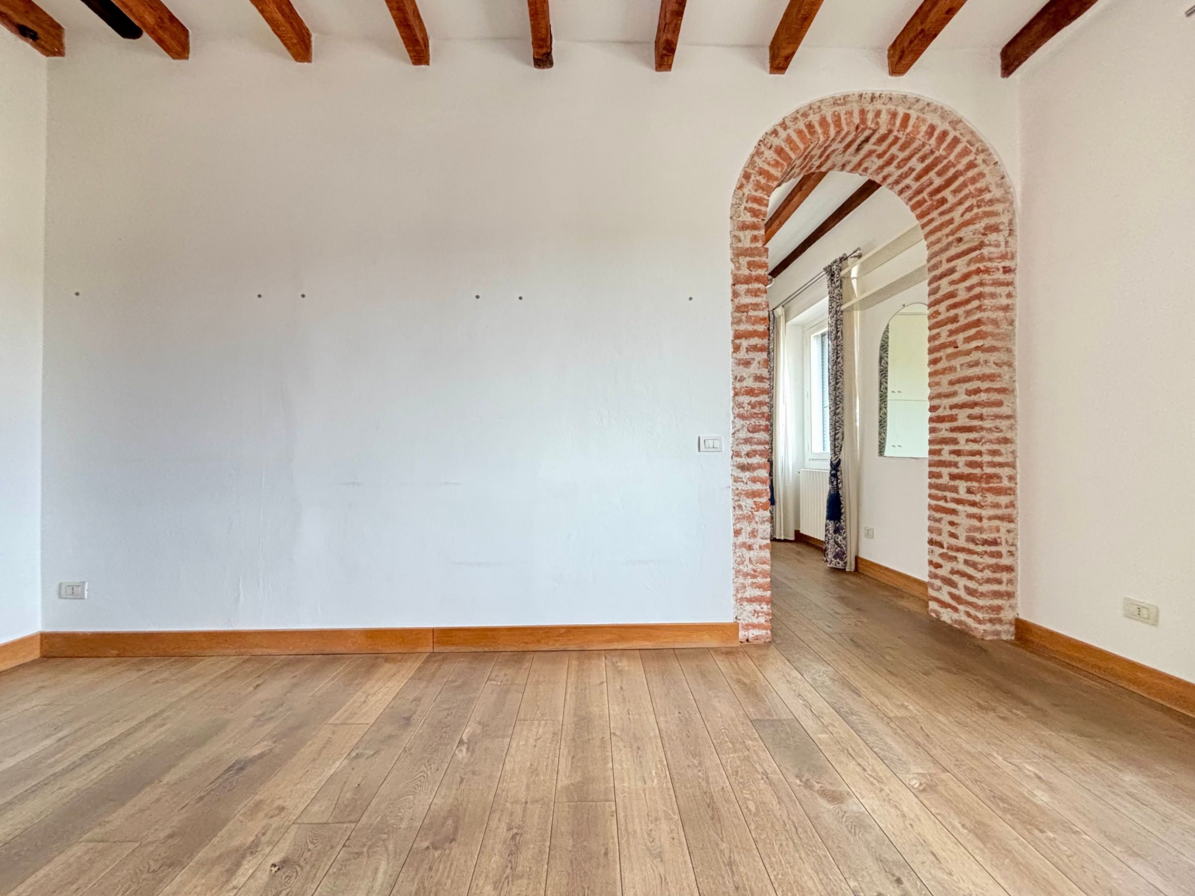 muro bianco, porta ad arco con mattoni a vista, travi a vista