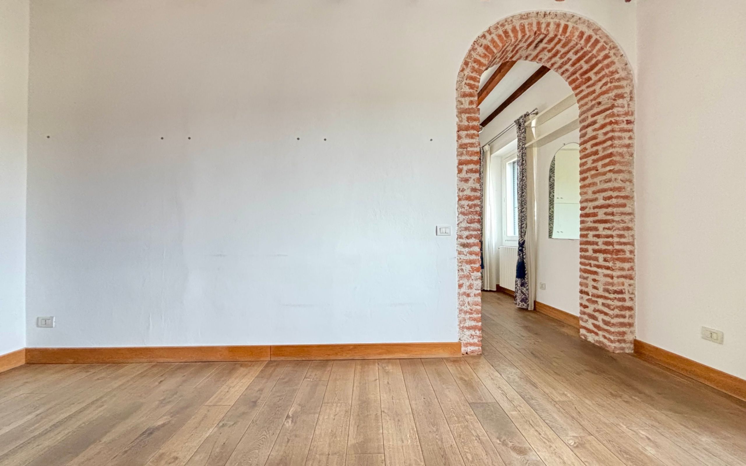 muro bianco, porta ad arco con mattoni a vista, travi a vista