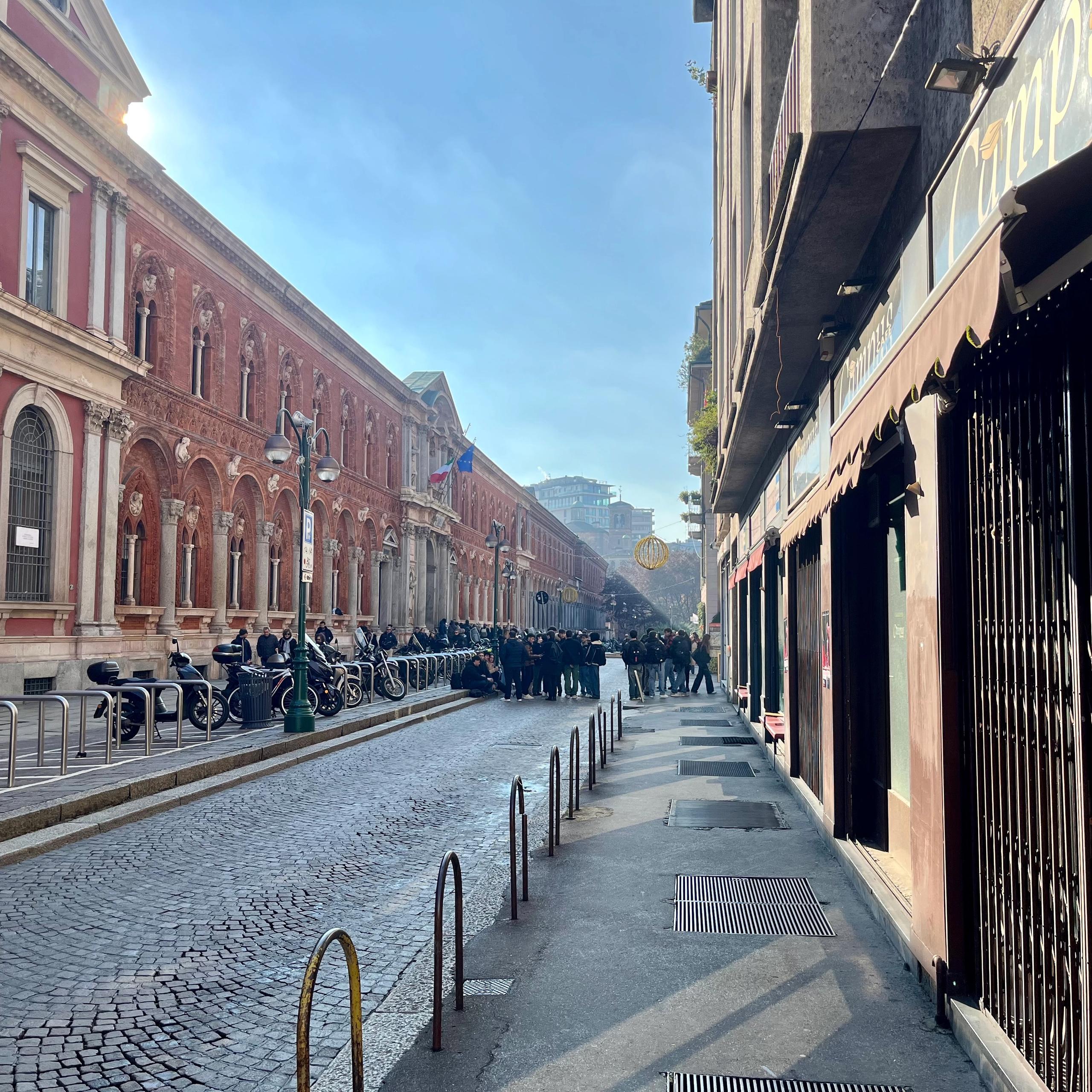 facciata di un bar di fronte alla statale di Milano, saracinesche chiuse, vetrine chiuse, locale chiuso, marciapiede, pavè, edifici con finestre e balconi