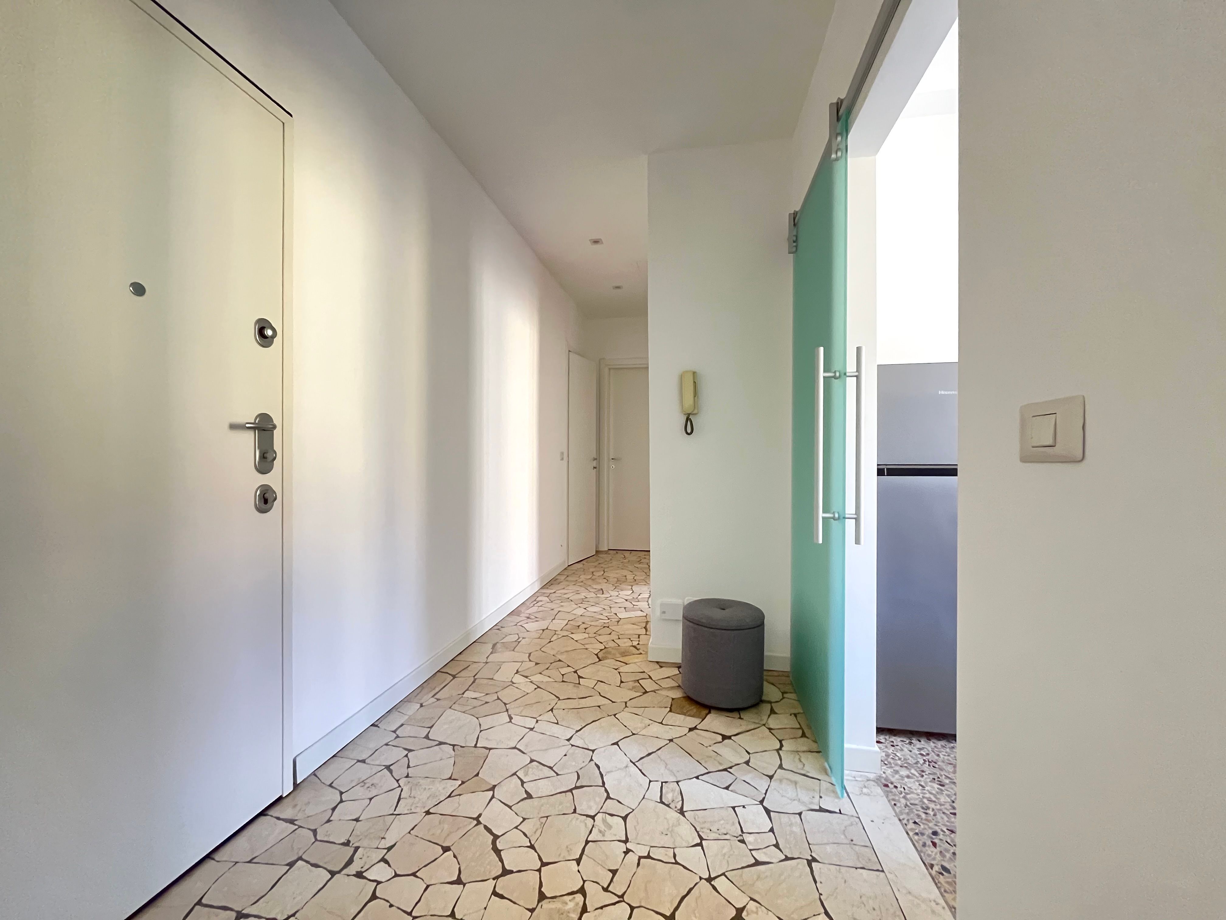 corridioio con seminato veneziano, cestino della spazzatura, porta di accesso alla cucina, frigorifero e porta di ingresso
