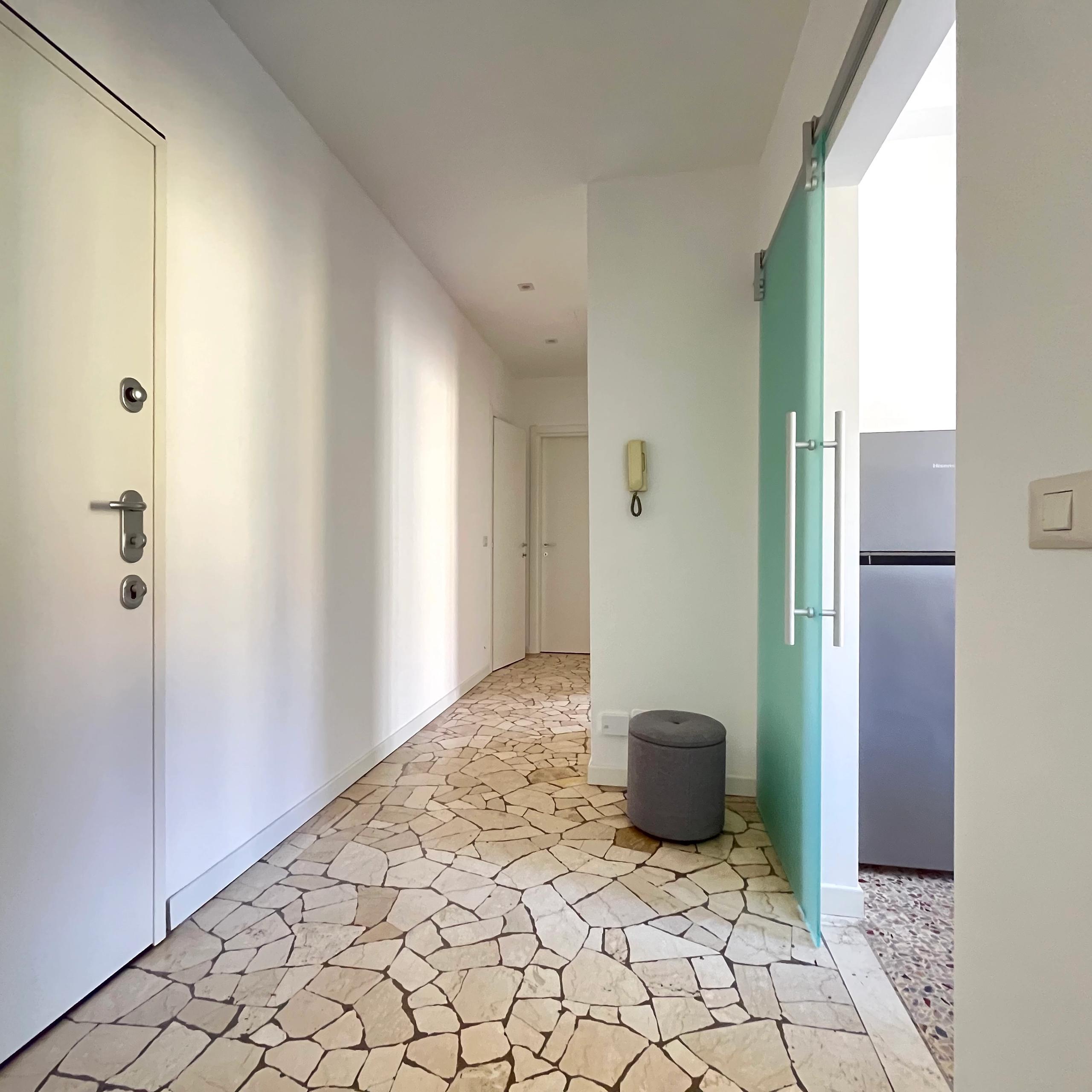 corridioio con seminato veneziano, cestino della spazzatura, porta di accesso alla cucina, frigorifero e porta di ingresso