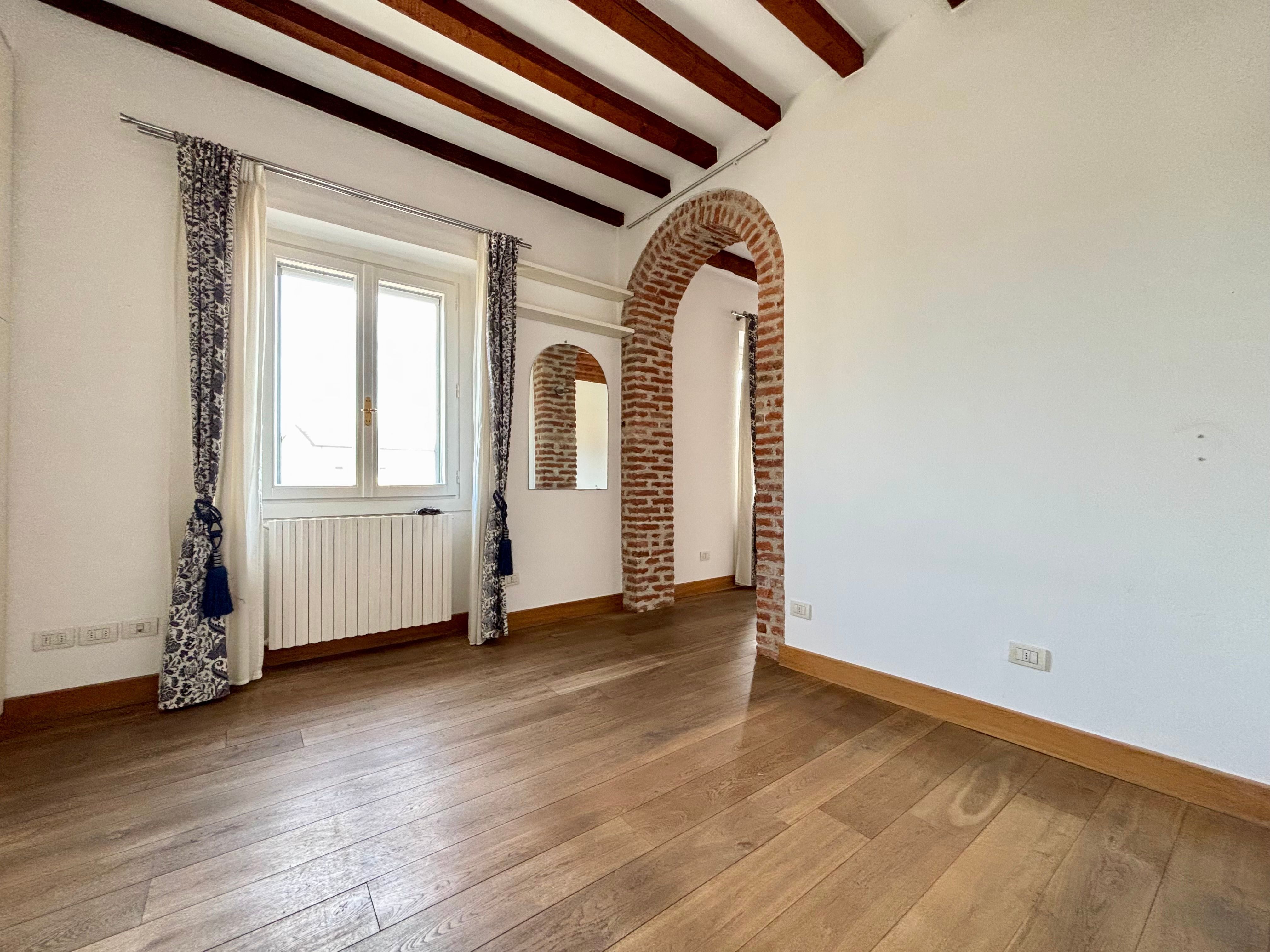 muro bianco, porta ad arco con mattoni a vista, travi in legno a vista, finestra con tende