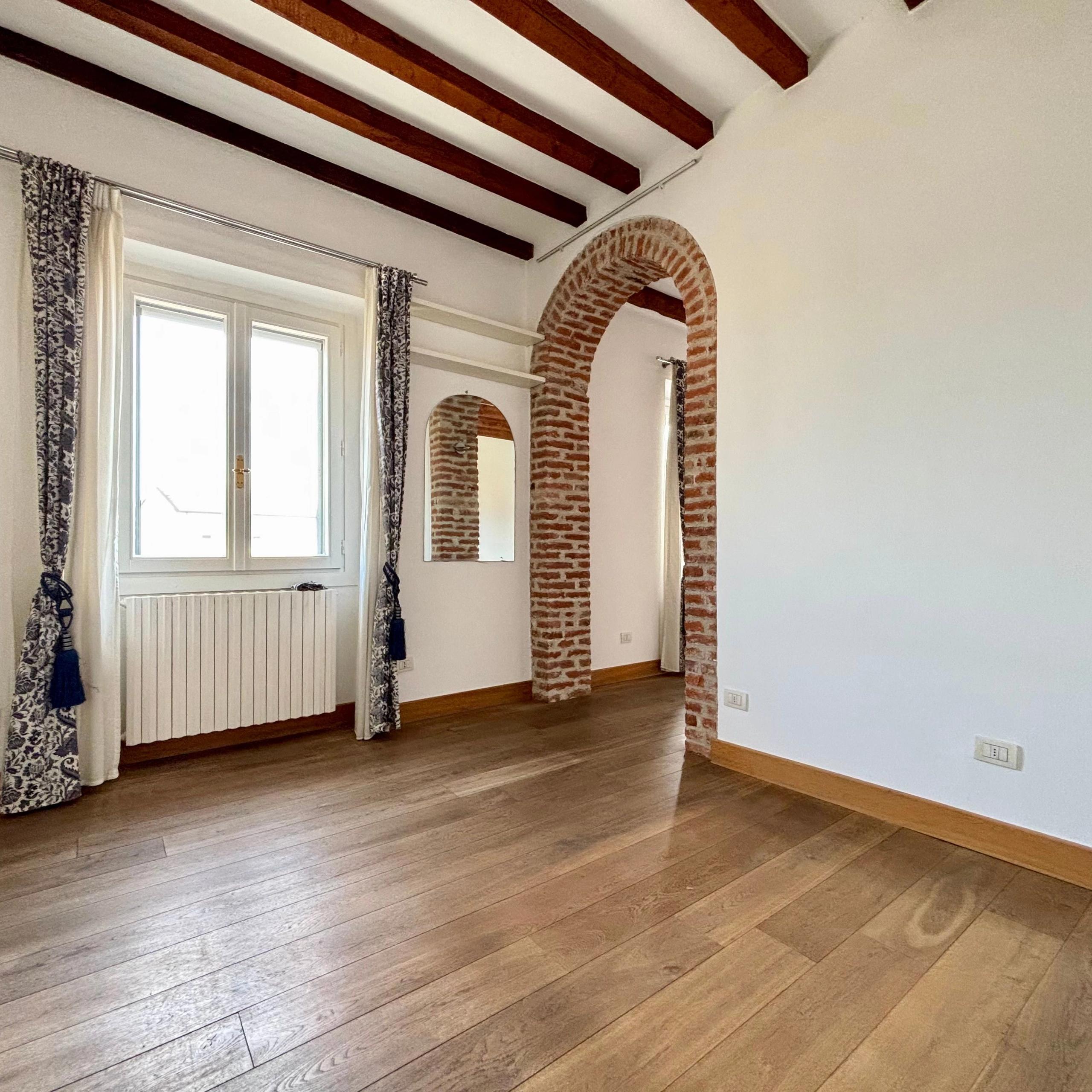 muro bianco, porta ad arco con mattoni a vista, travi in legno a vista, finestra con tende