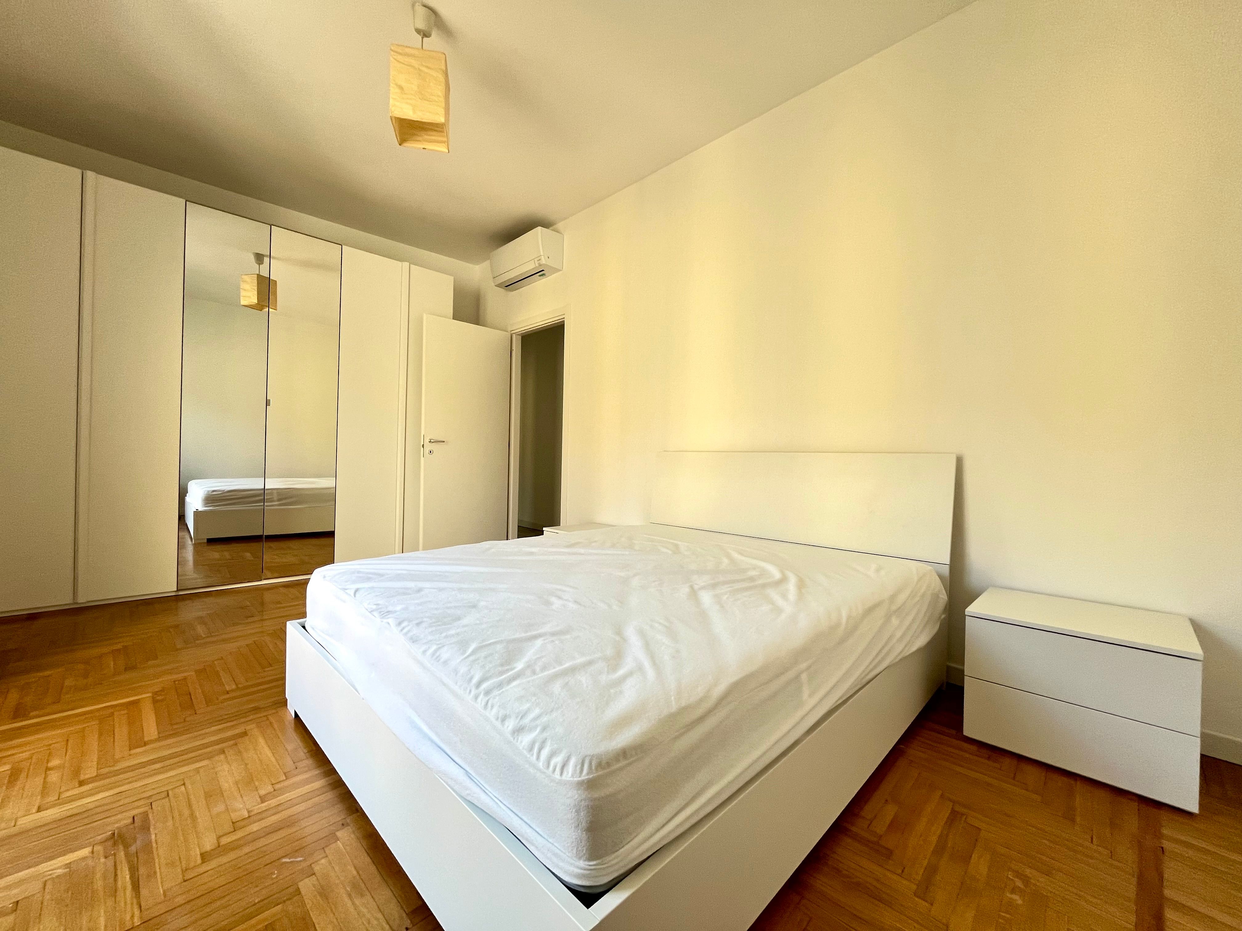 camera da letto con pavimento in parquet, comodini, armadi e specchio, split aria condizionata