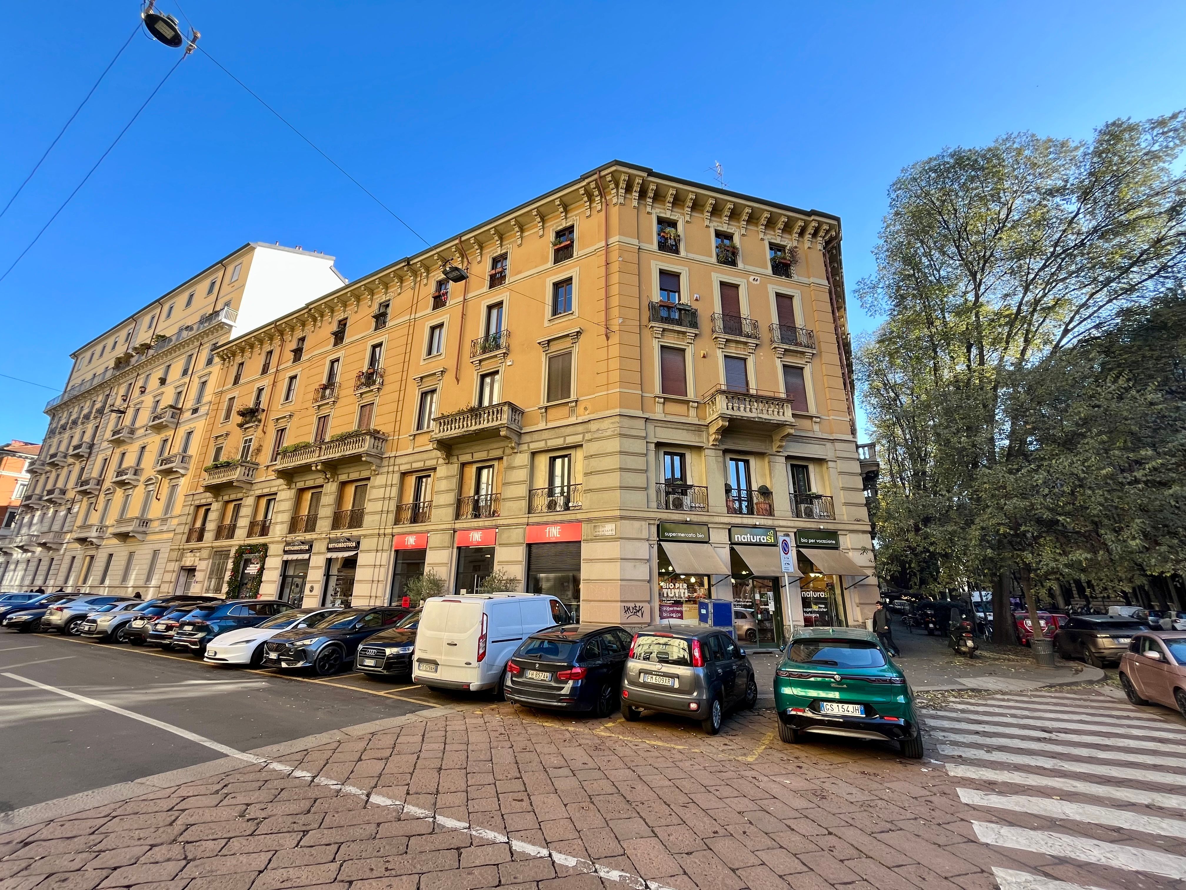 Street with parked cars, Corner building, Shopfront display windows and residential windows, Tree-lined avenue