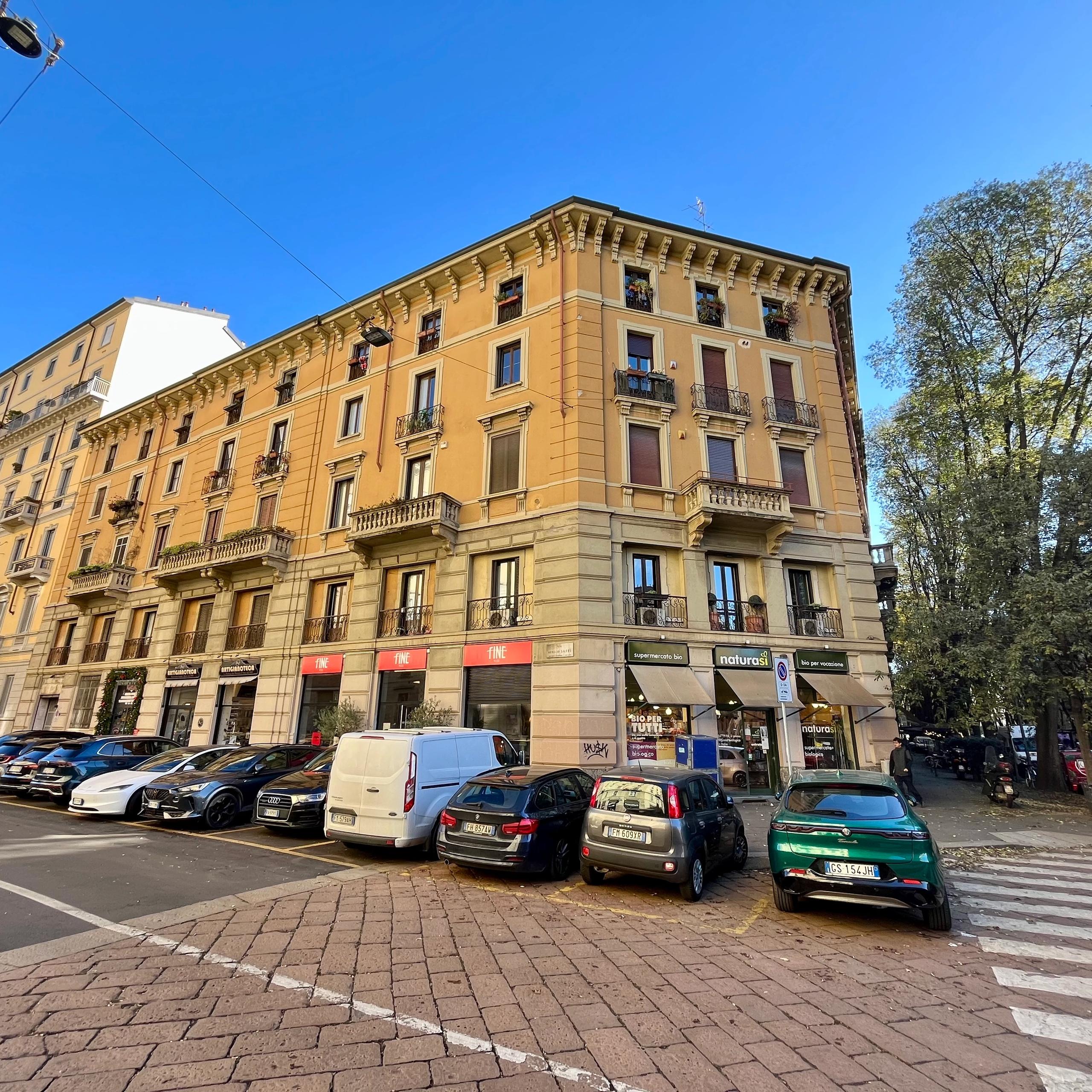 Street with parked cars, Corner building, Shopfront display windows and residential windows, Tree-lined avenue