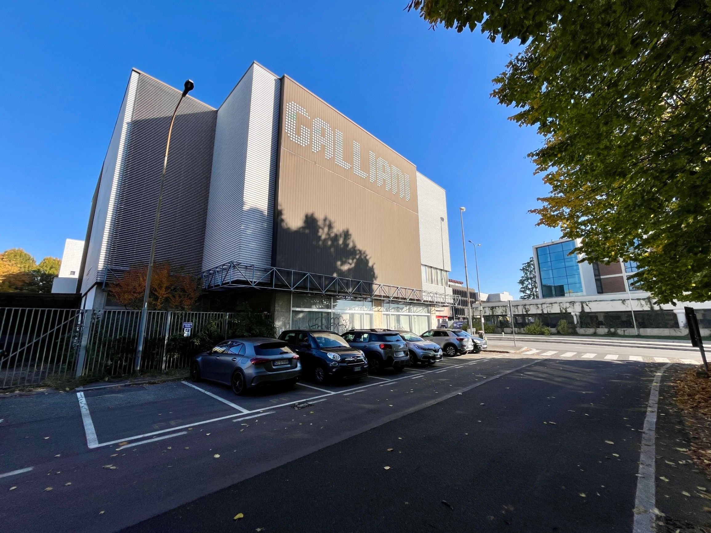 building with parking and cars, trees and sky, street