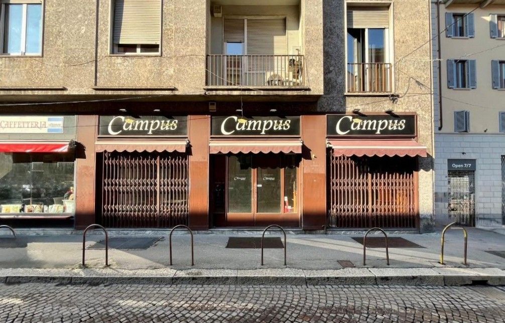facciata di un bar di fronte alla statale di Milano, saracinesche chiuVetrine chiuse, locale chiuso, marciapiede, pavè, edifici con finestre e balconi